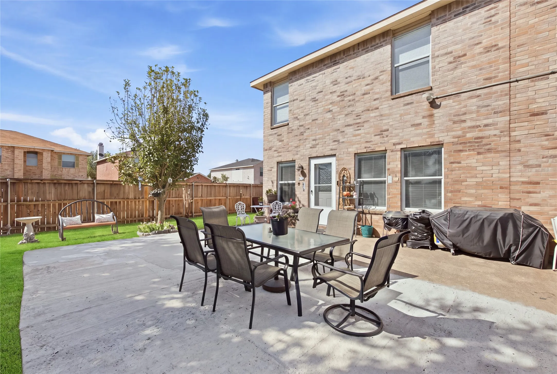 Expansive concrete patio with direct access to the interior, complemented by a manicured lawn and a full privacy fence