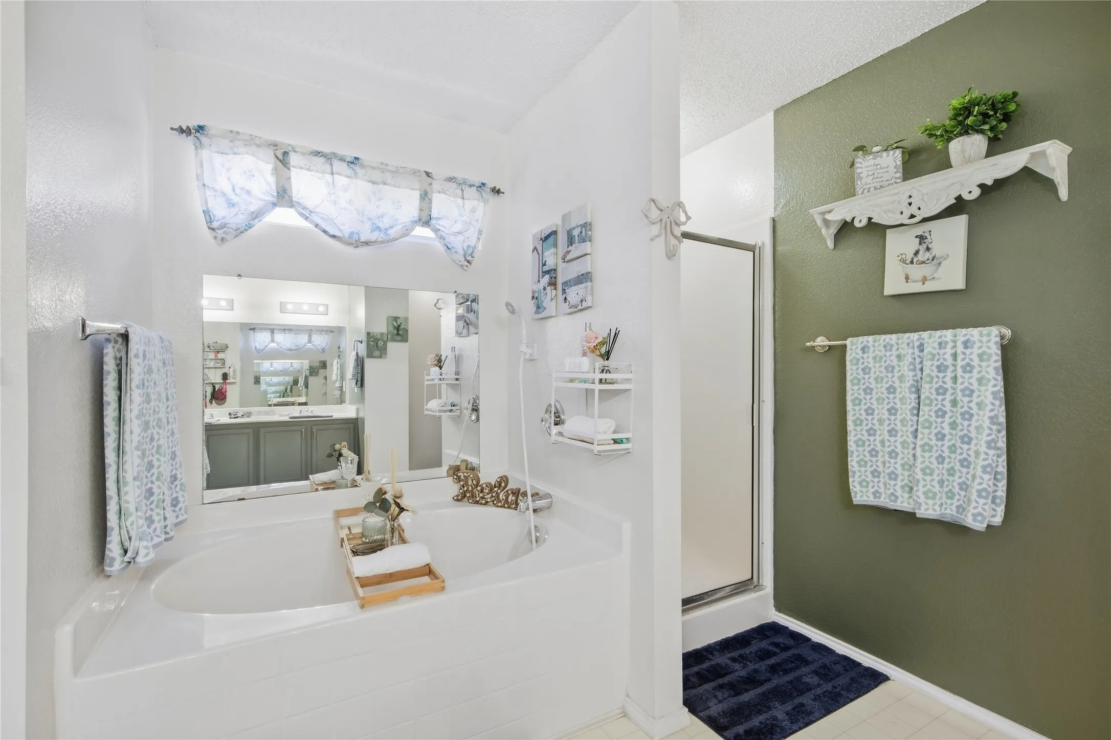Built-in soaking tub, large vanity mirror, recessed overhead lighting, glass-enclosed shower, and a wall-mounted towel bar