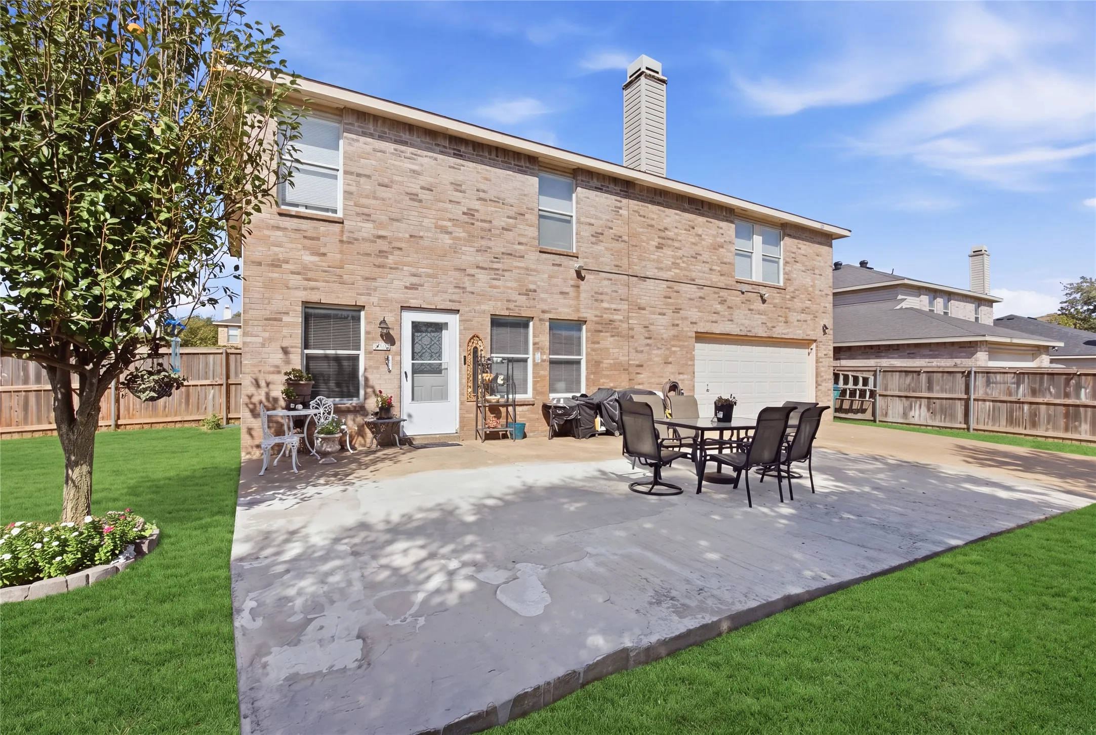 Brick exterior, concrete patio, two-car garage, manicured lawn, and wood privacy fence