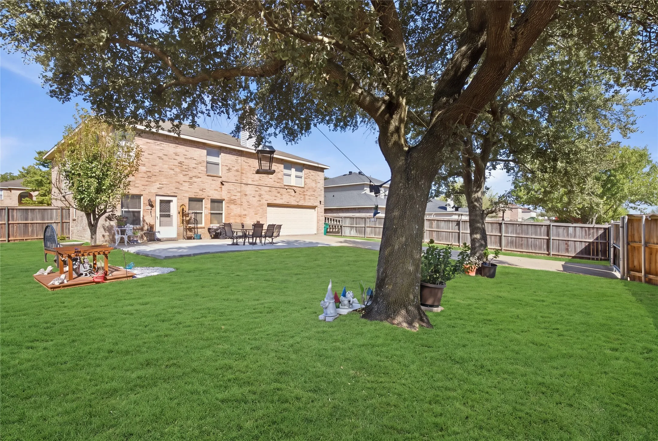 Expansive backyard featuring a large mature tree, a privacy fence, and a concrete patio