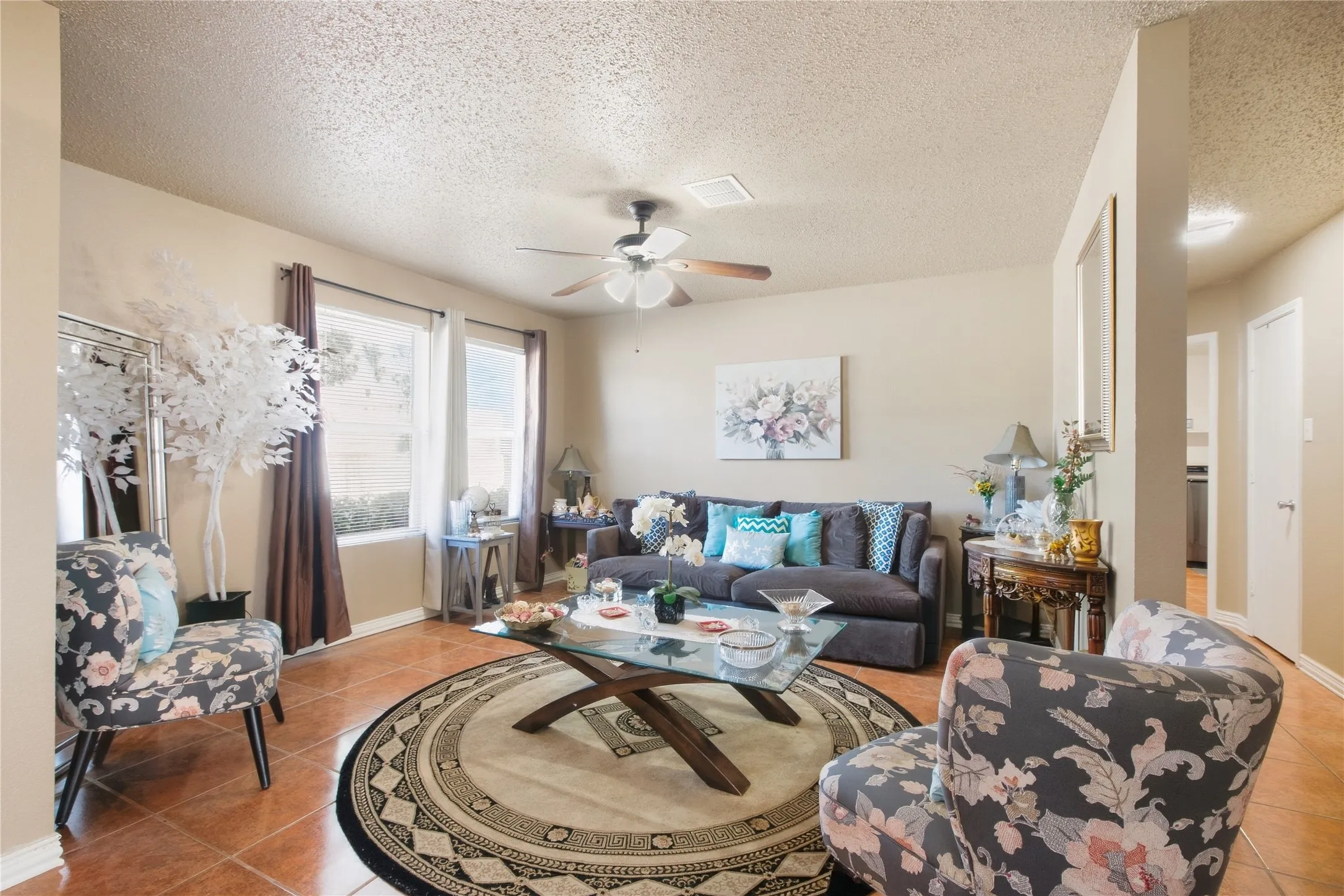Living area featuring tile flooring, neutral wall tones, a ceiling fan, and multiple windows