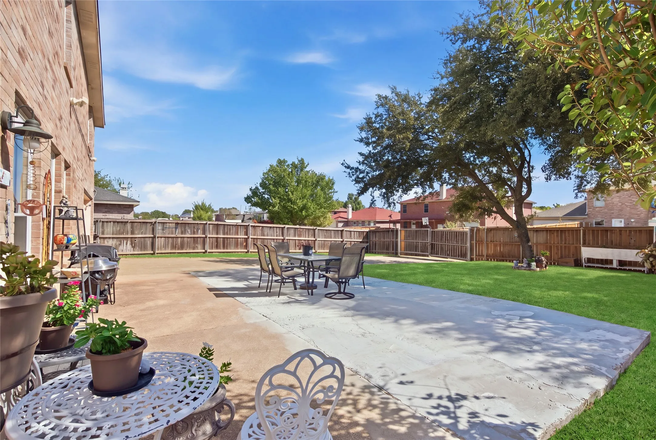 Expansive backyard featuring a brick exterior, concrete patio, lush green lawn, and a mature shade tree