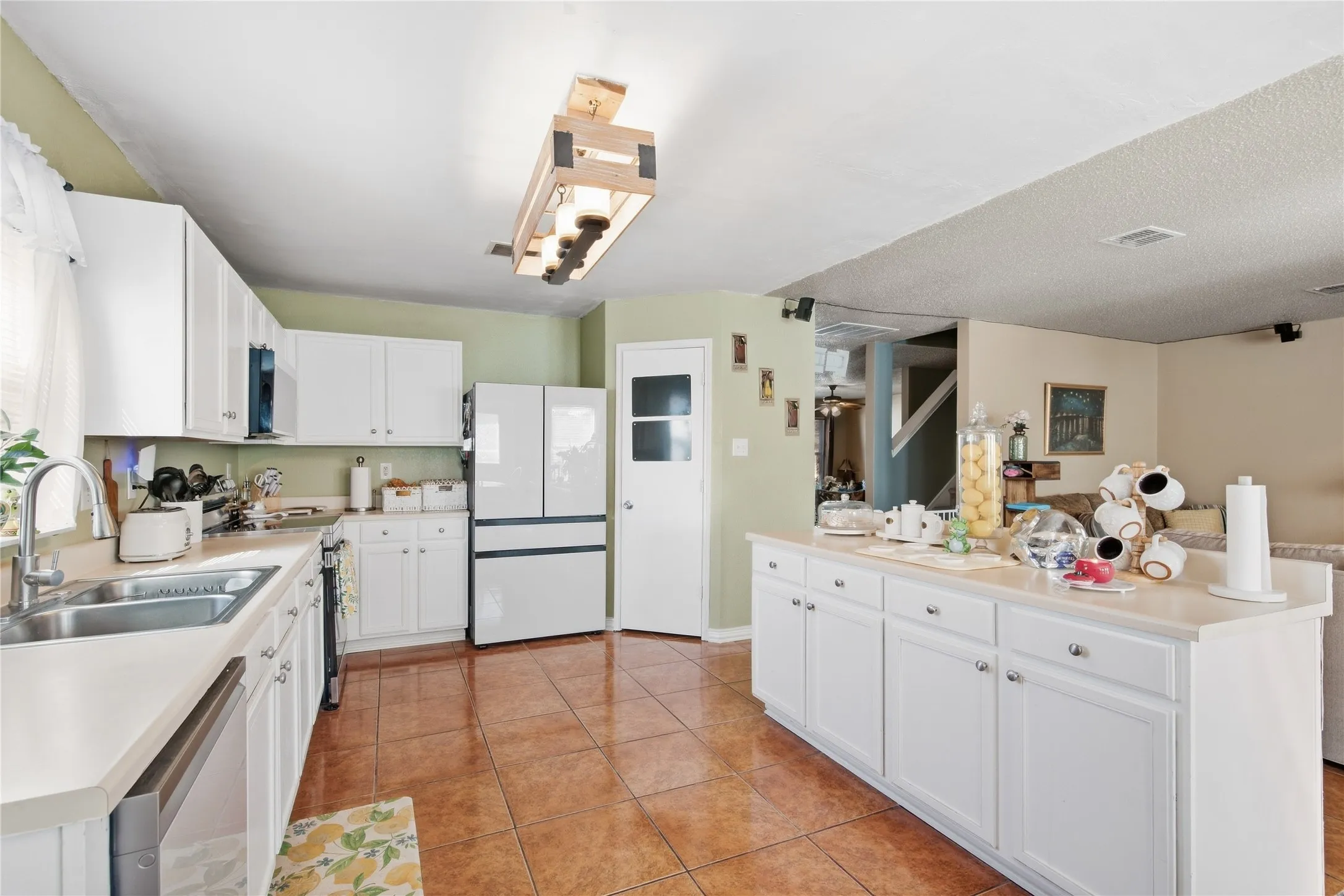 Kitchen featuring white cabinetry, light-toned countertops, a stainless steel sink, and tile flooring