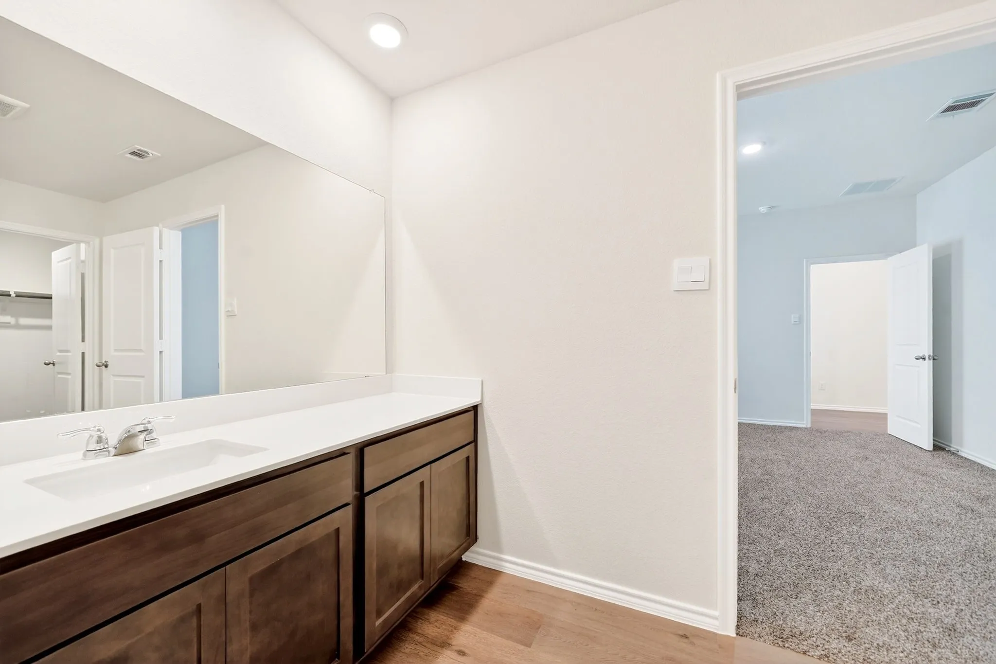 Wood-finish flooring, recessed lighting, expansive vanity with integrated sink, white countertop, and dark wood cabinetry