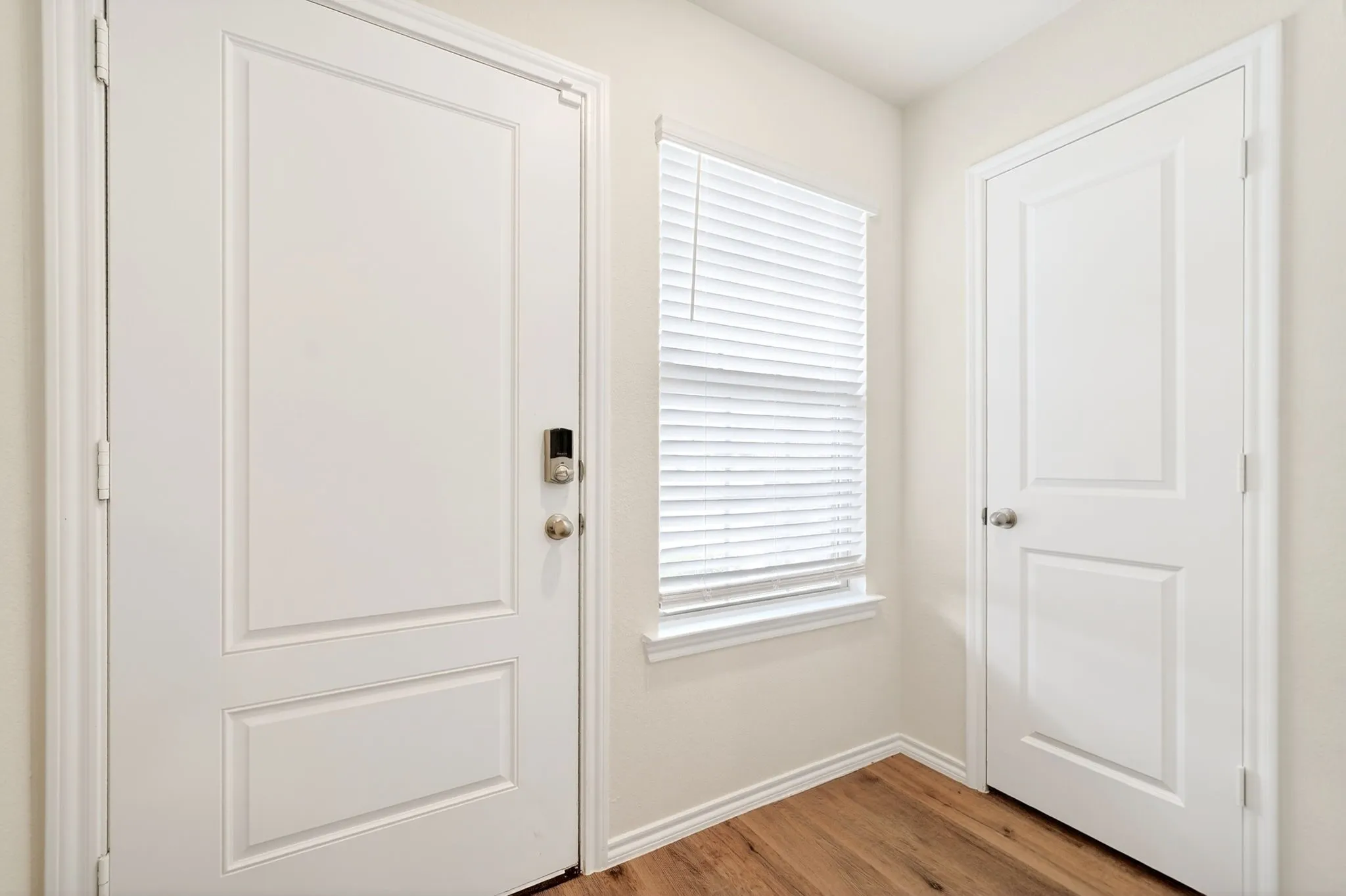 Entryway with wood-finish flooring, white panel doors, and a window with blinds