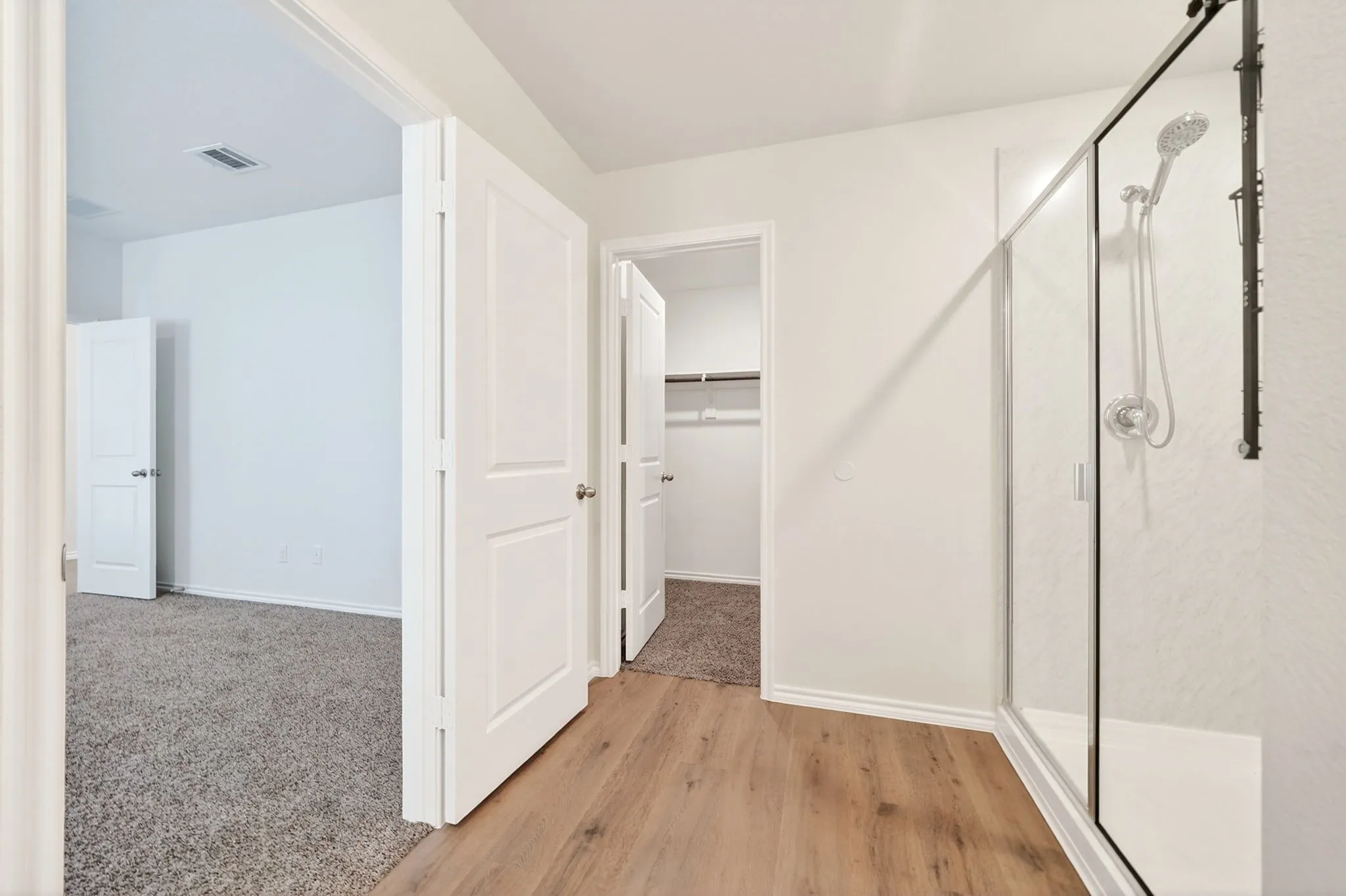Glass-enclosed shower with a handheld showerhead, wood-finish flooring, and white interior doors