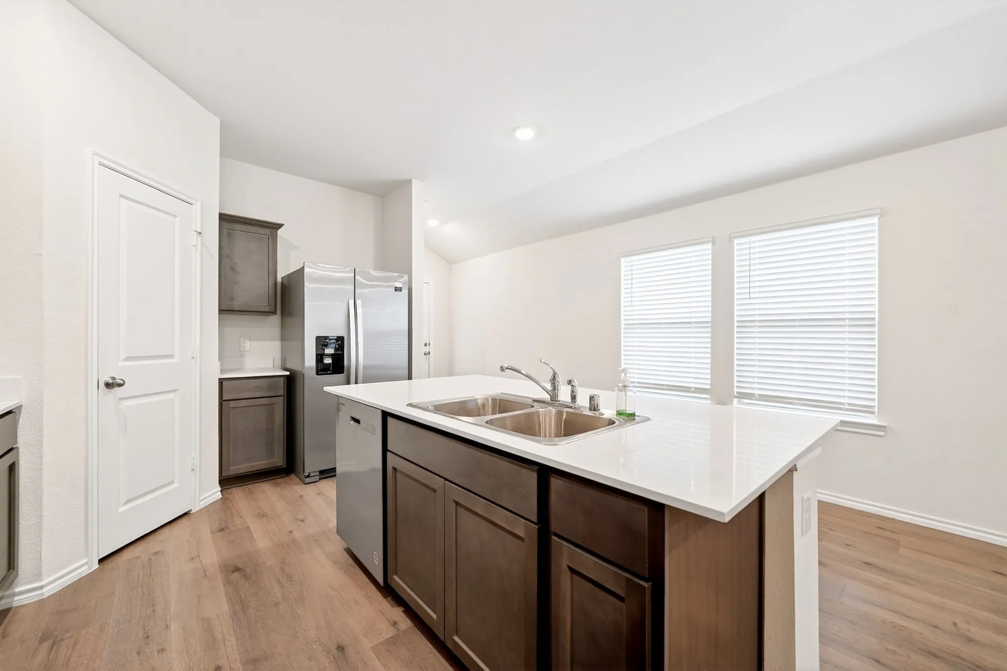 Kitchen featuring wood-finish flooring, white countertops, dark wood-finish cabinetry, and a double basin sink with a gooseneck faucet