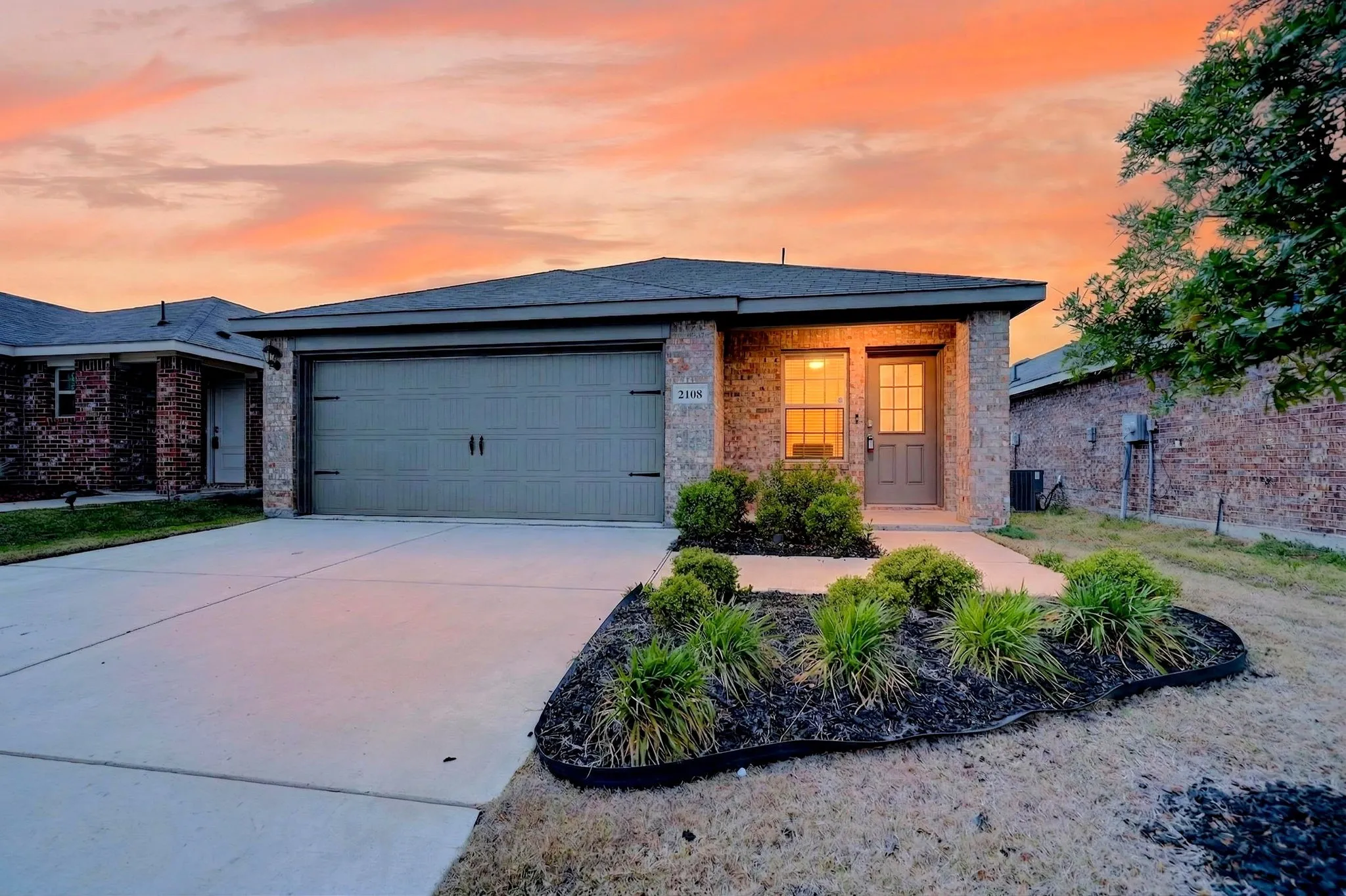 Brick exterior with a covered entry, attached garage, and landscaped front yard