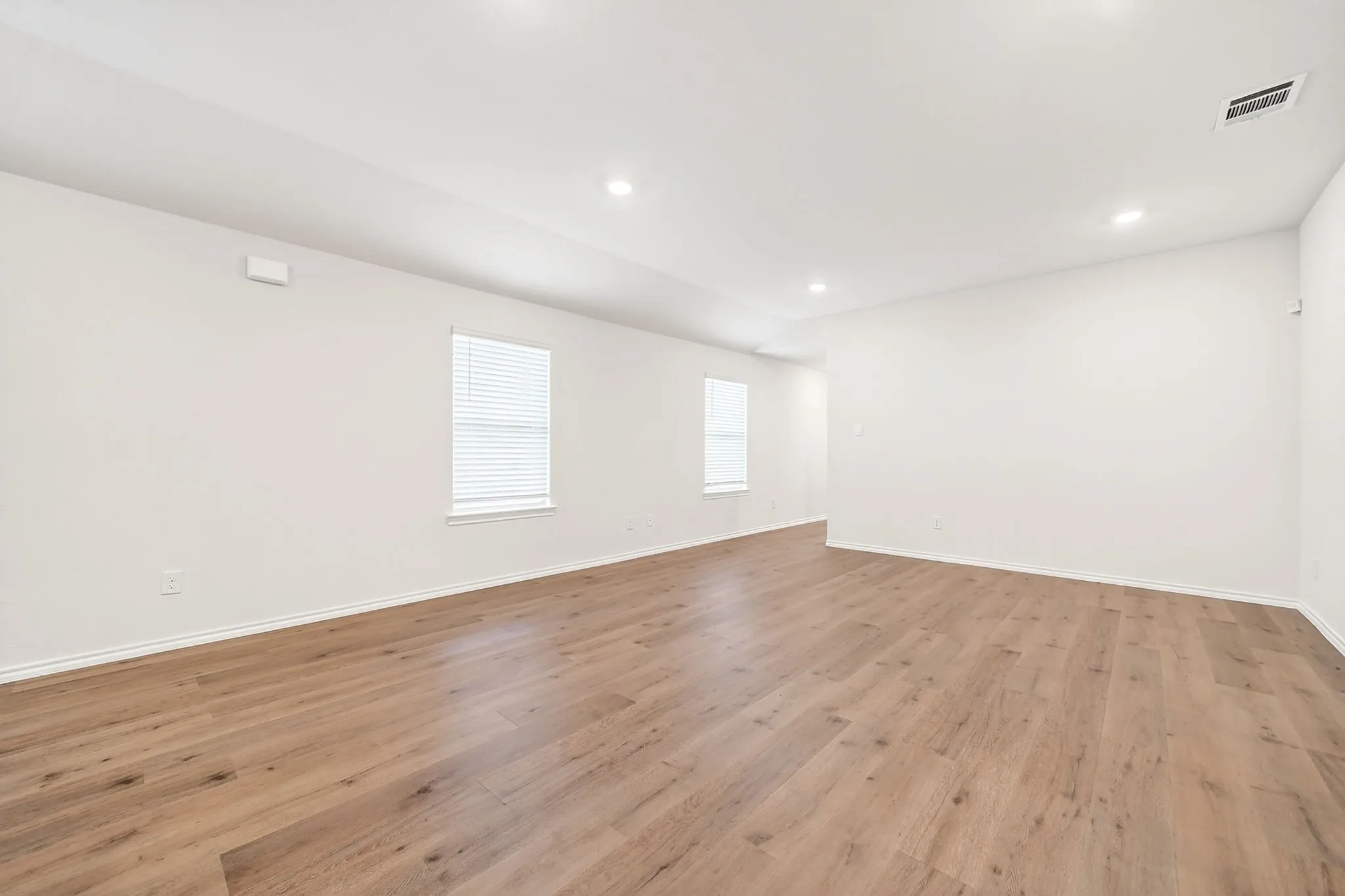 Spacious room with wood-finish flooring, recessed lighting, and multiple windows with blinds