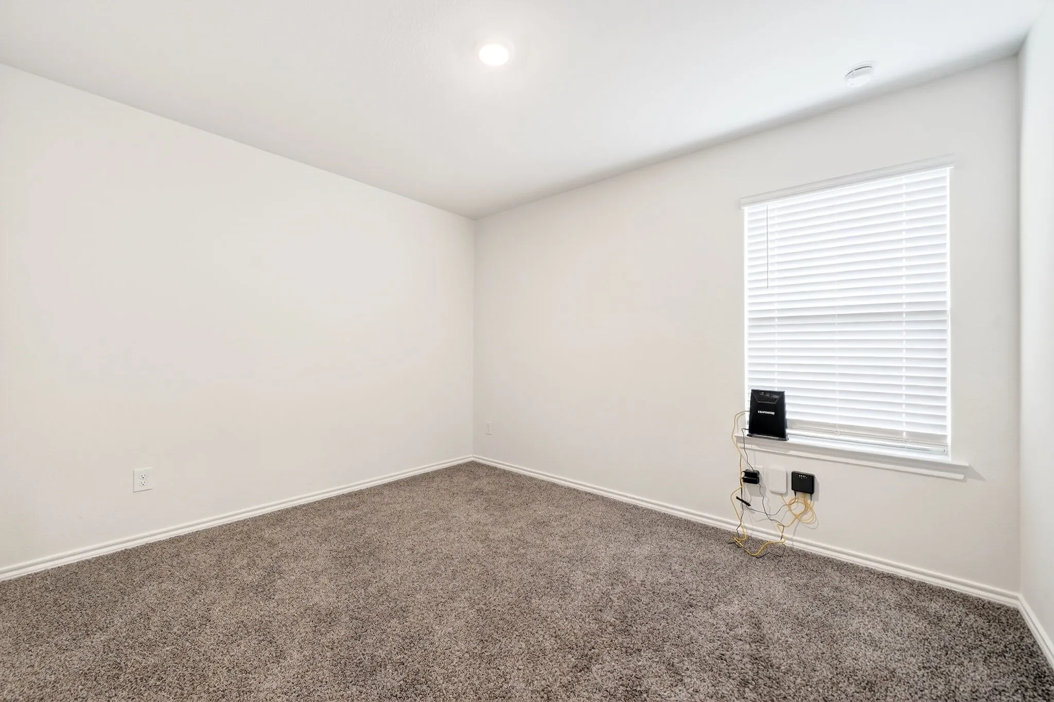 Neutral wall color with recessed lighting, window with blinds, and textured carpet