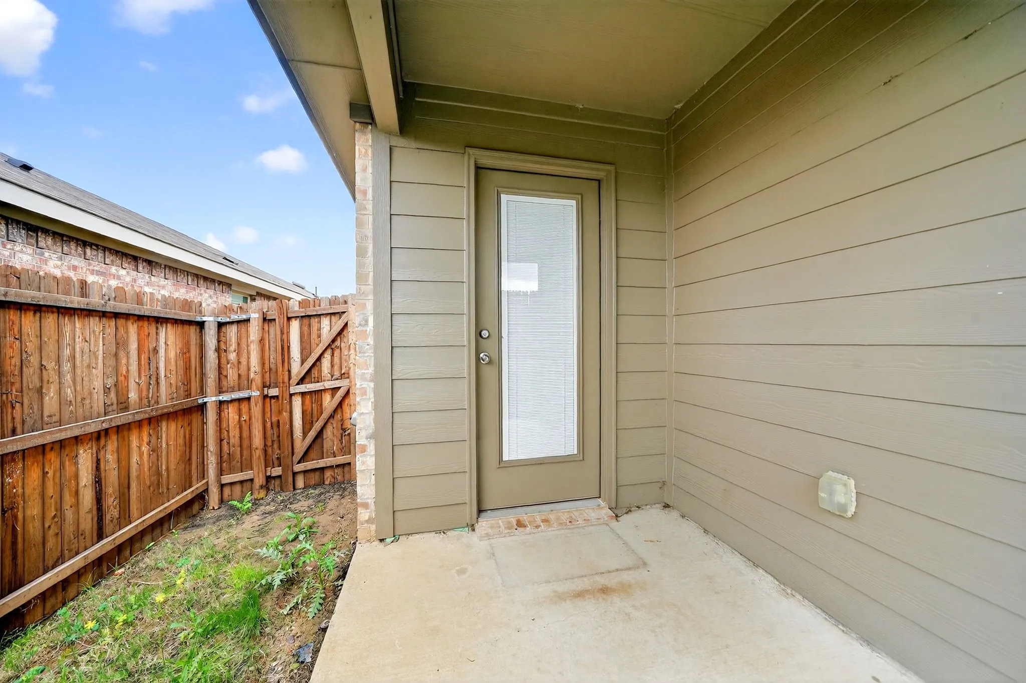 Private outdoor patio with a solid privacy fence, concrete paving, and a glass-paneled exterior door