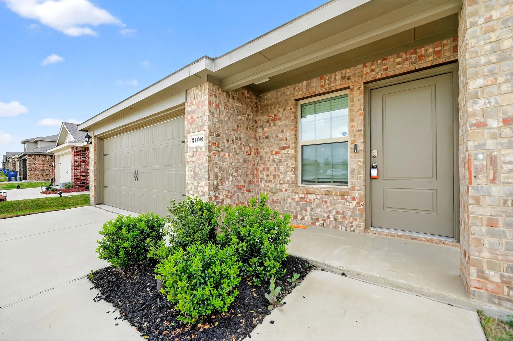 Brick exterior with a paneled front door, an attached garage, and established landscaping