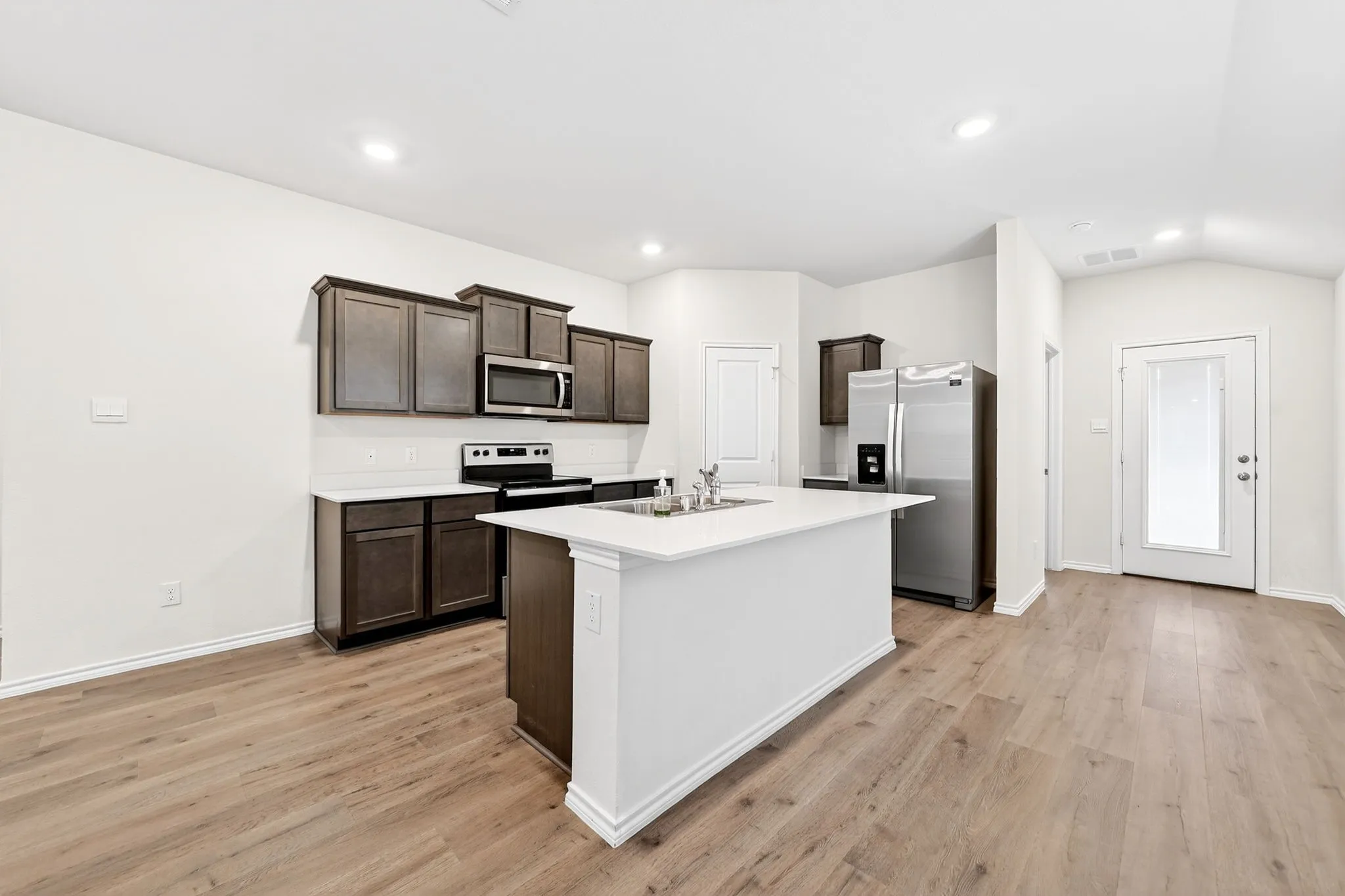Kitchen with wood-finish flooring, dark wood cabinetry, white countertops, a central island, and stainless steel appliances
