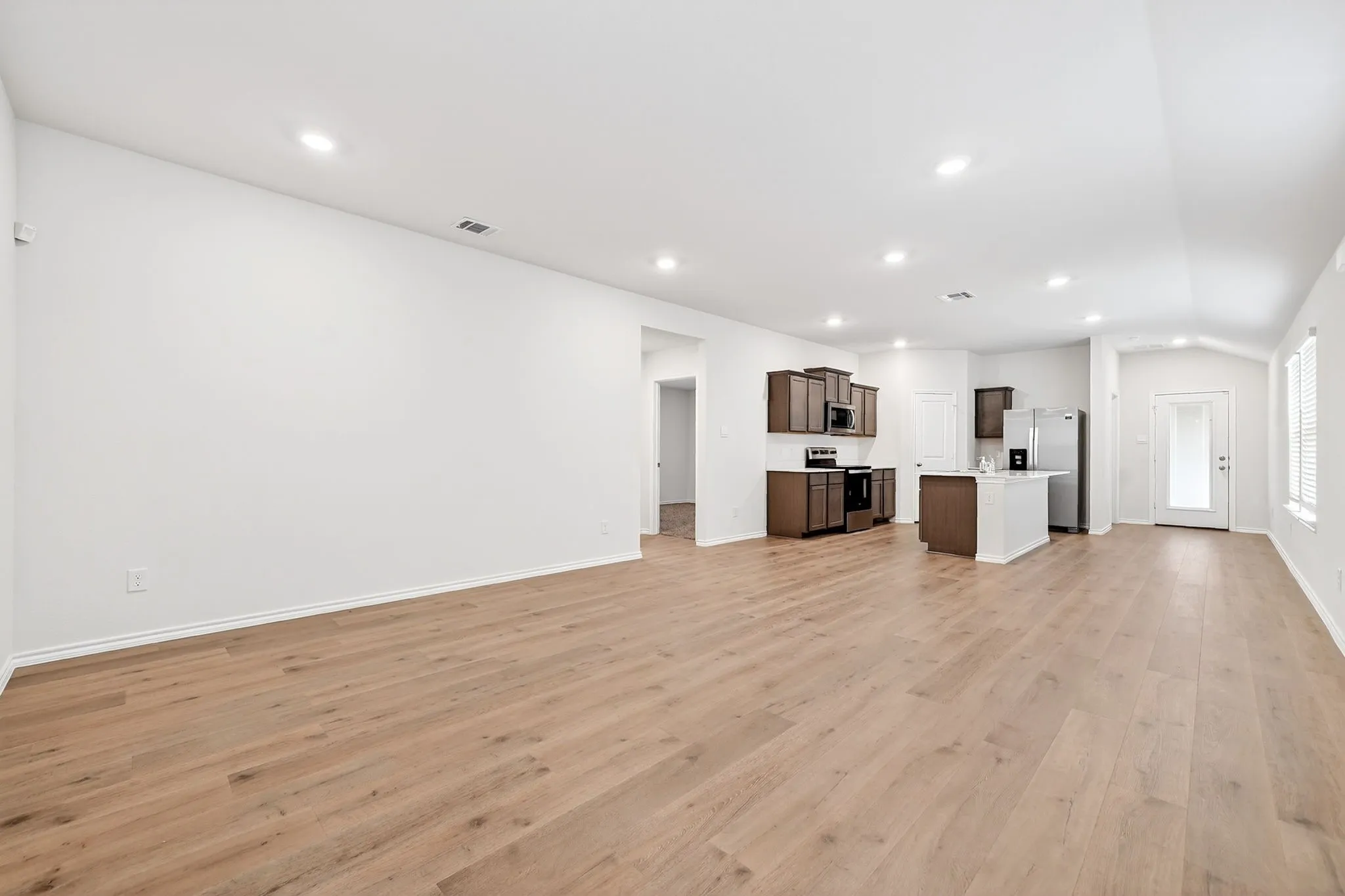 Expansive living area with wood-finish flooring, recessed lighting, and an open-concept kitchen featuring dark wood cabinetry and a central island