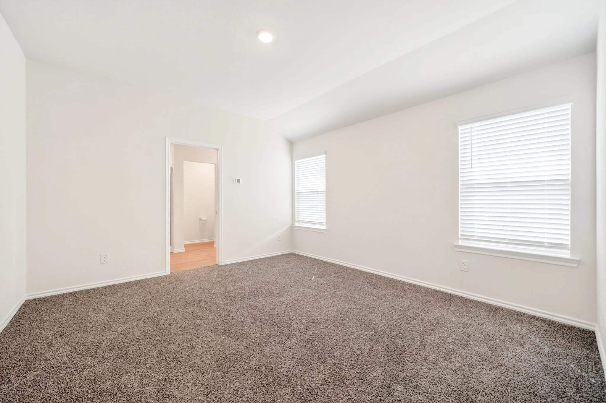 Recessed lighting, neutral wall paint, two windows with blinds, and carpeting