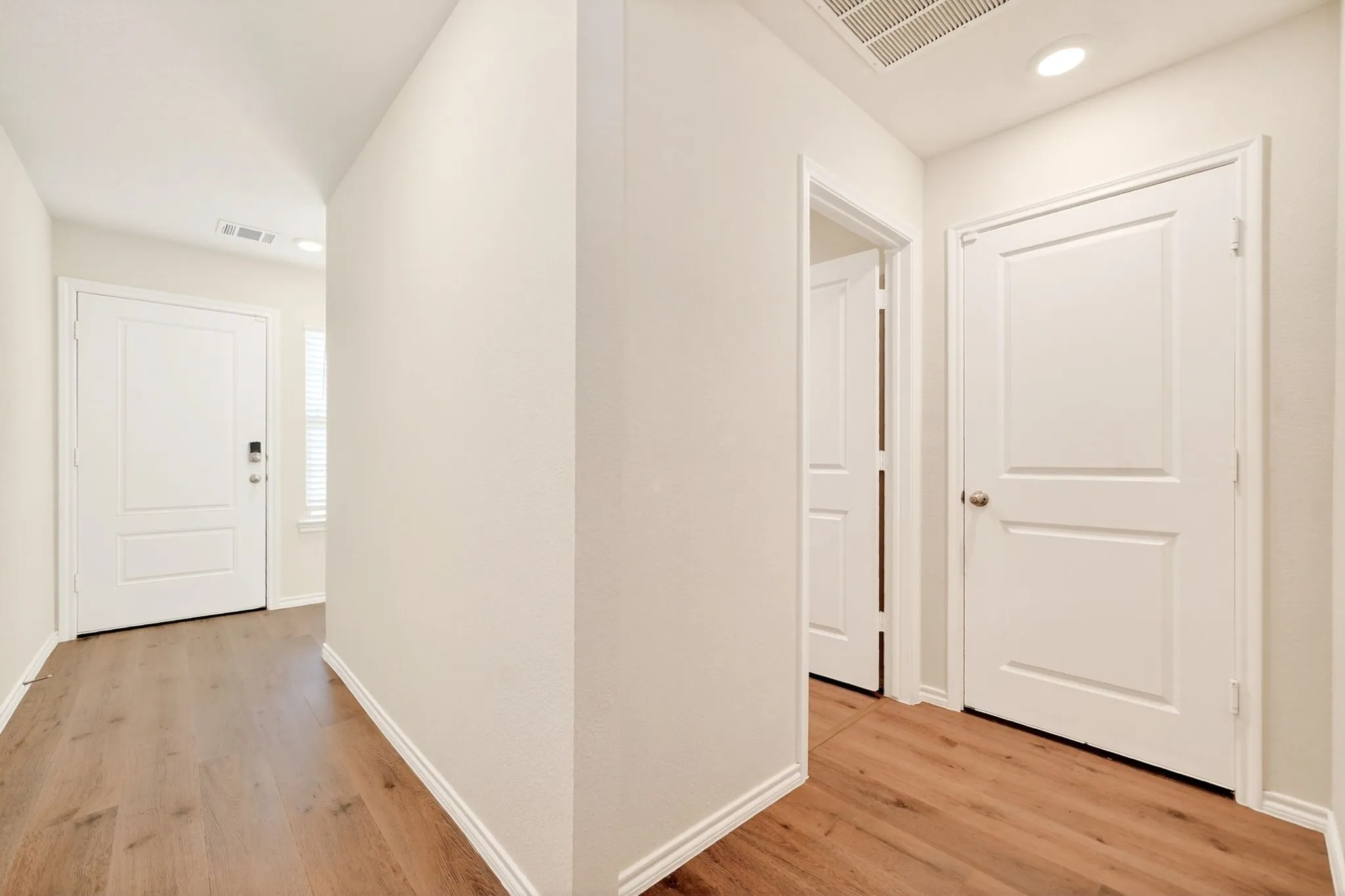 Wood-finish flooring throughout, bright white doors with panel detailing, recessed ceiling lighting, and neutral wall tones