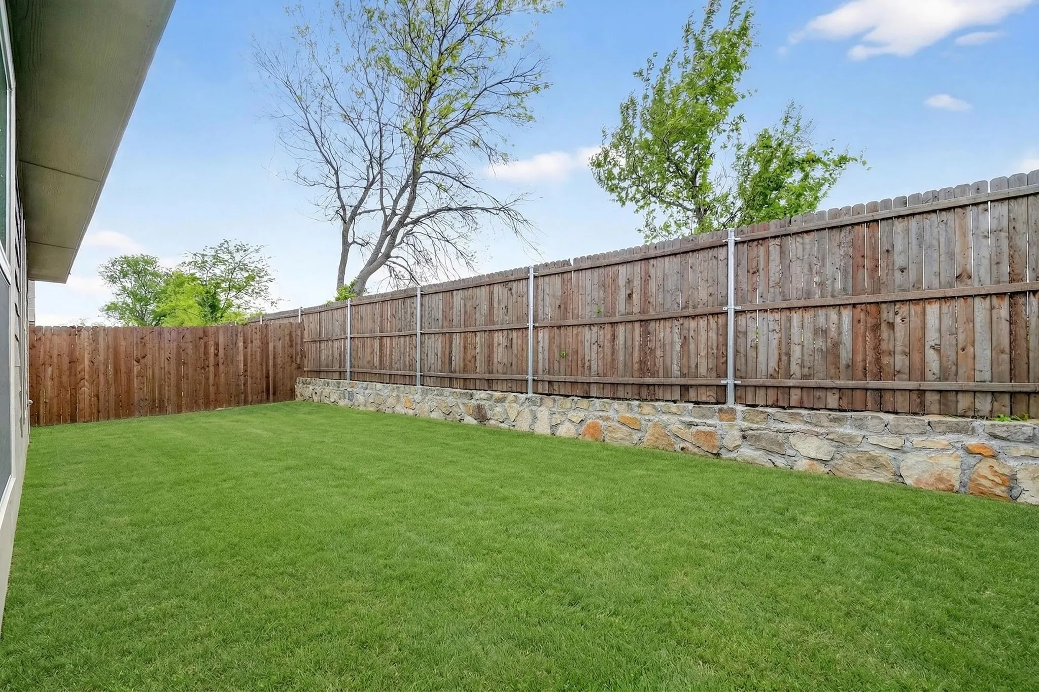 Expansive grassy yard with a natural stone retaining wall and wood privacy fencing