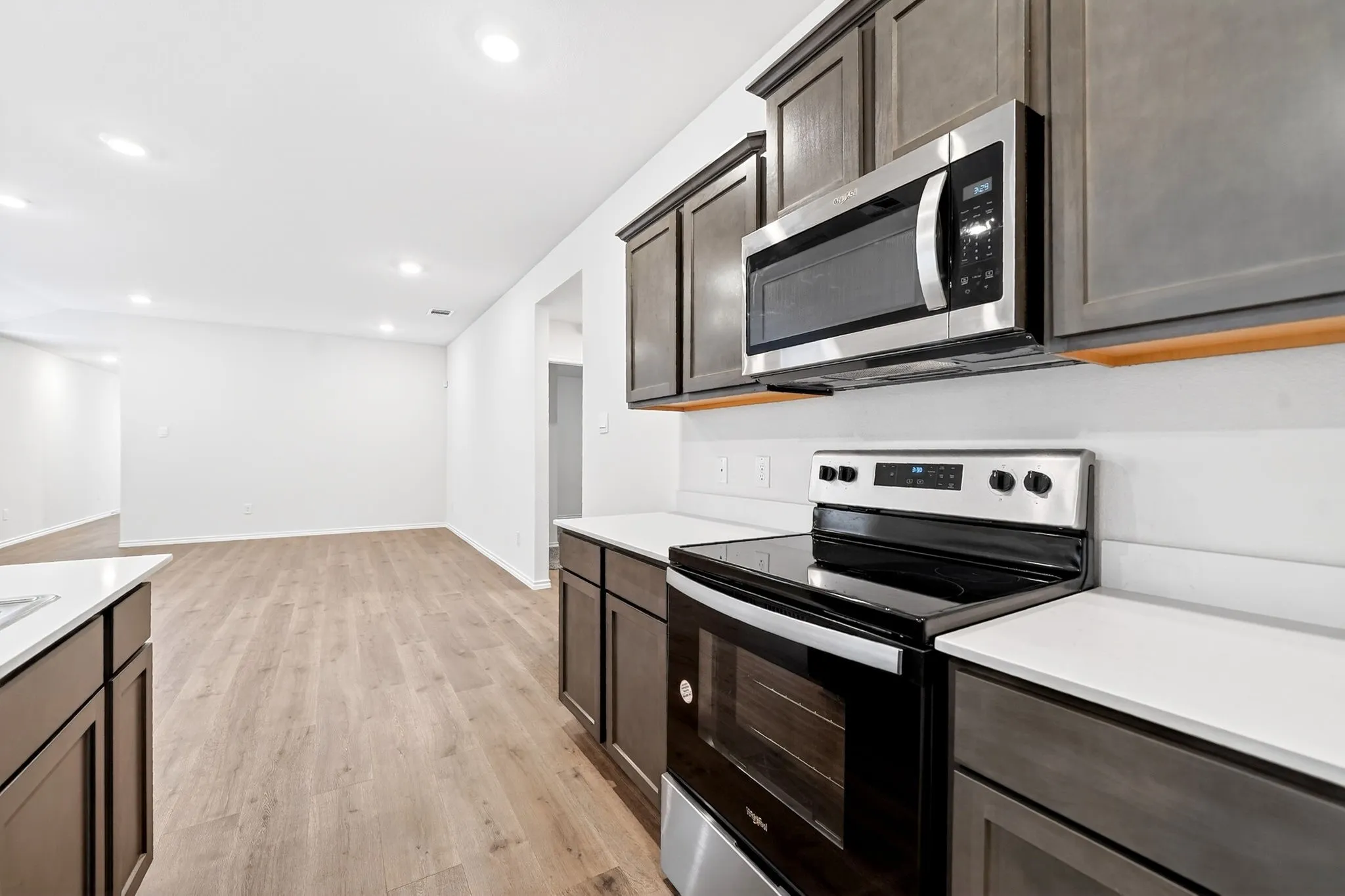 Dark wood-finish cabinetry, stainless steel appliances, white countertops, and wood-finish flooring