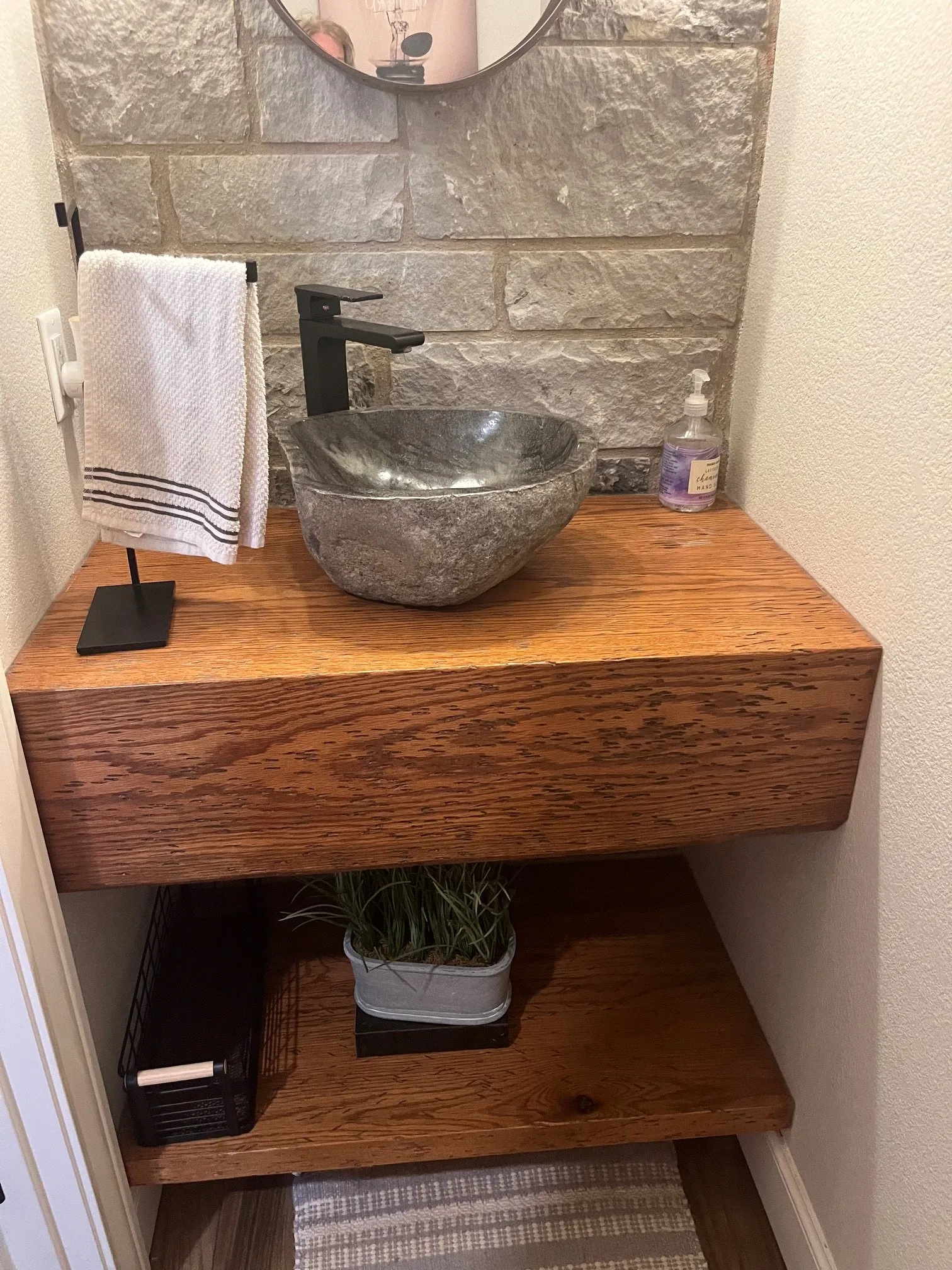 Floating wood-finish vanity with a vessel sink, matte black faucet, and stone-finish wall treatment