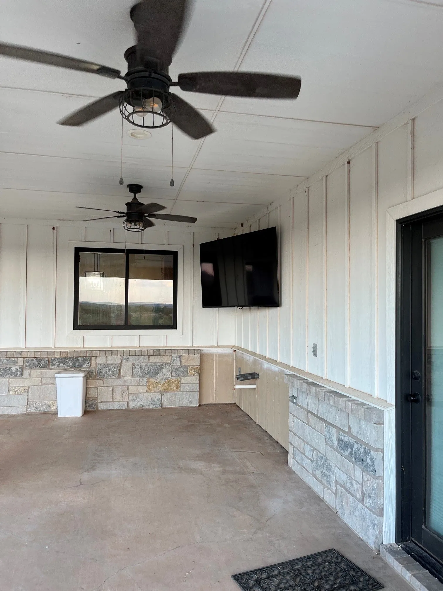 Covered patio with two ceiling fans, plank ceiling, board and batten siding, and stone veneer accents