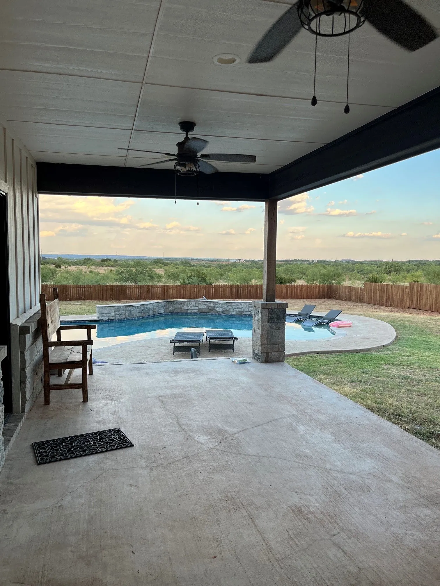 Expansive covered patio with concrete flooring, dual ceiling fans, and stone-clad support pillars