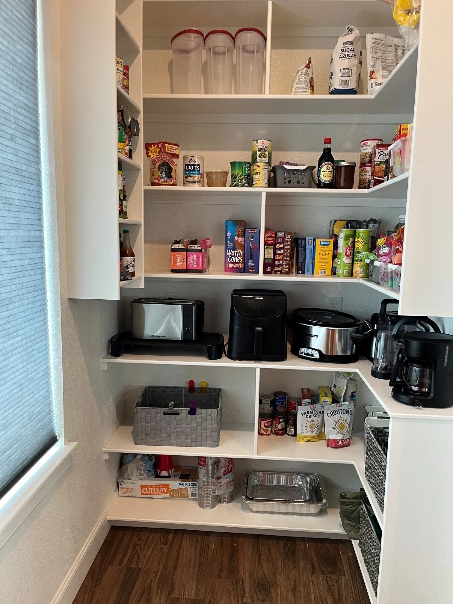 Corner pantry with extensive built-in shelving, wood-finish flooring, and natural light from a window