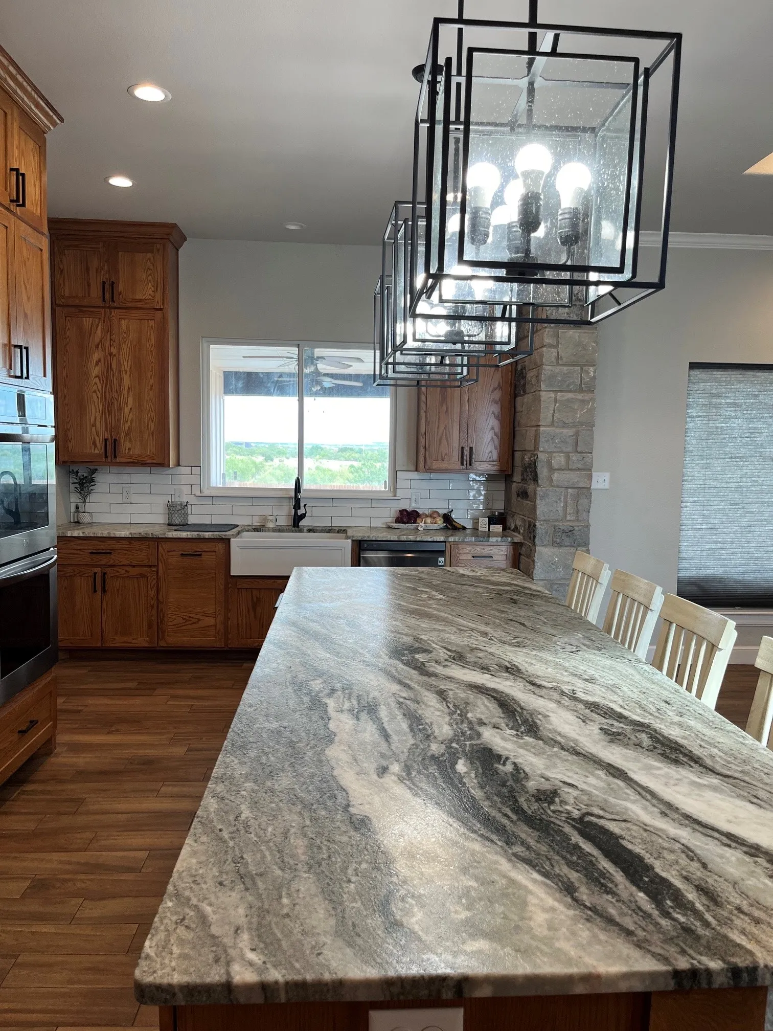 Expansive kitchen island with a patterned countertop, wood-finish flooring, recessed lighting, and a series of modern linear light fixtures