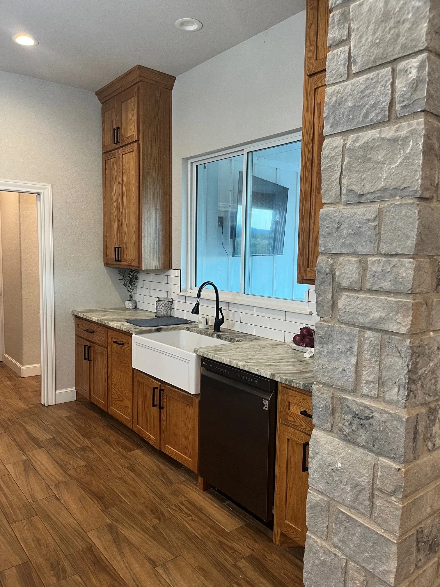 Kitchen featuring wood-finish cabinetry, a large apron-front sink, black appliances, stone countertops, and a subway tile backsplash