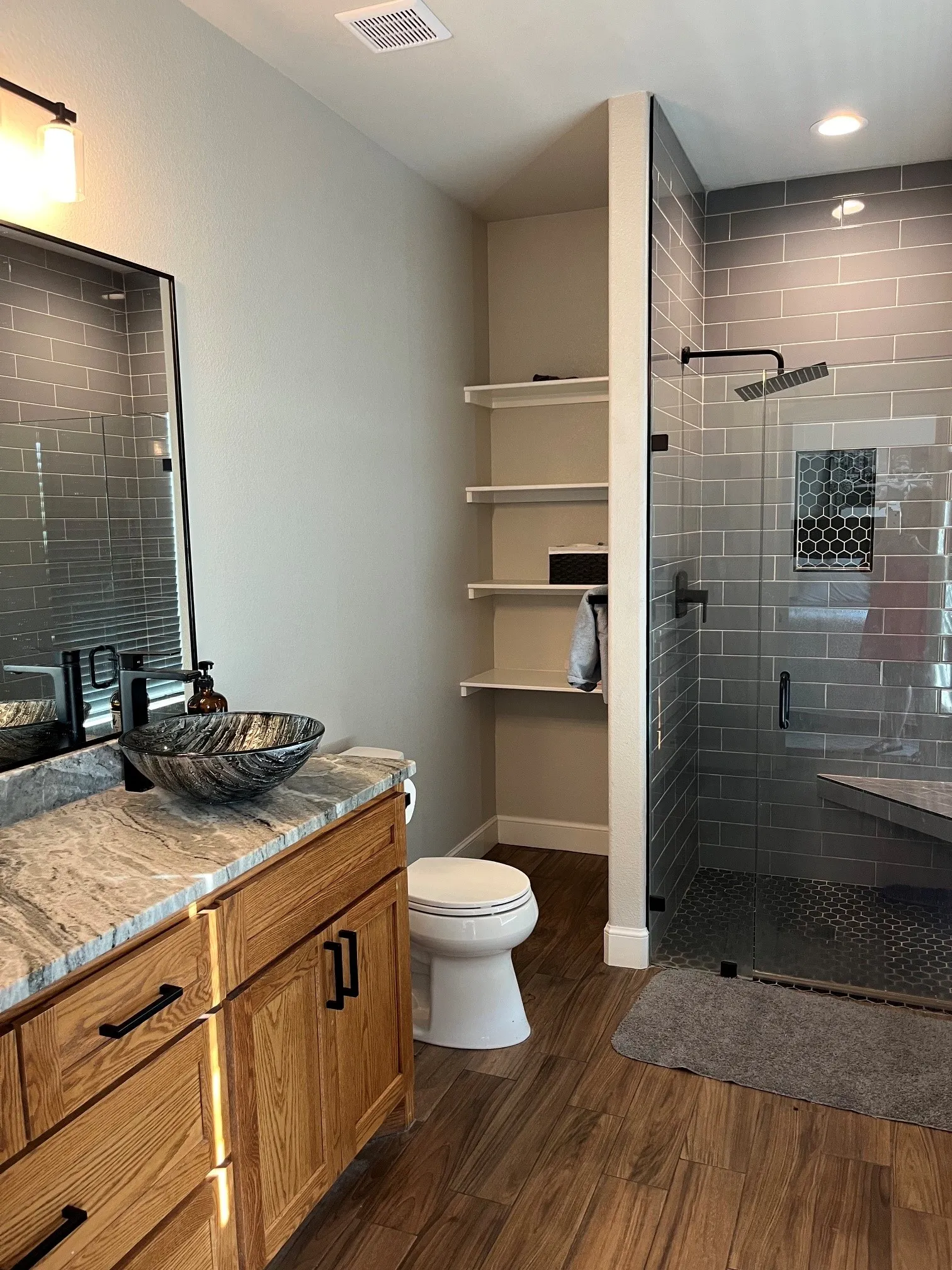 Wood-finish flooring, custom wood vanity with stone countertop, vessel sink, and an expansive walk-in shower with tiled walls and a built-in bench