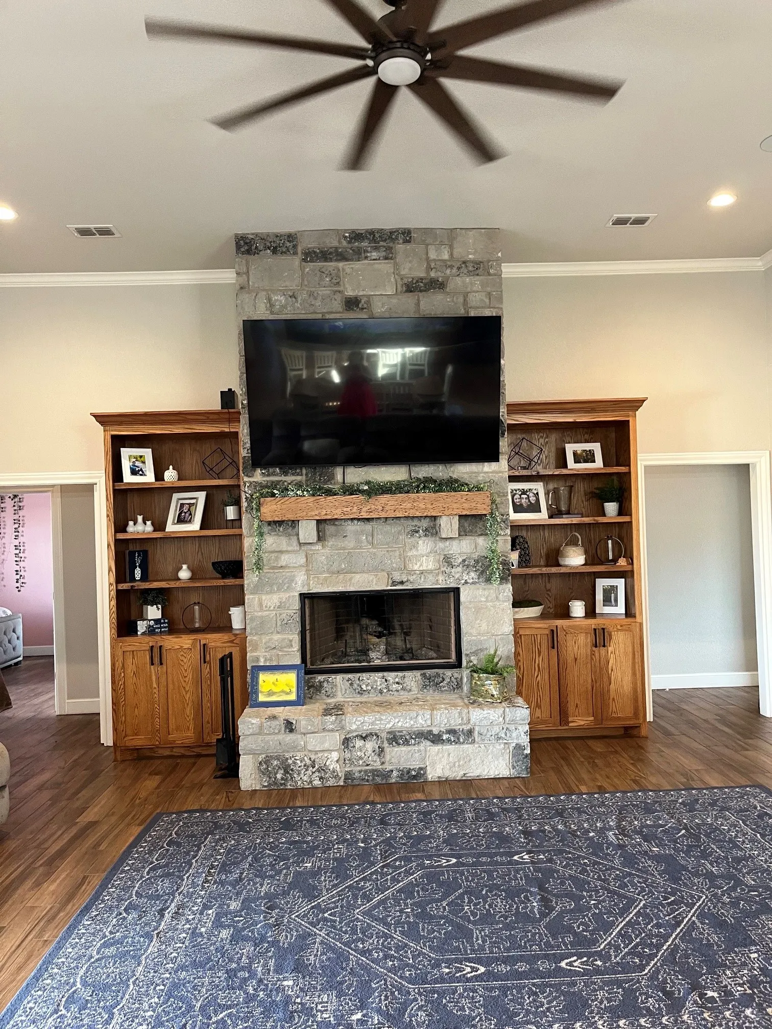 Stone fireplace with a wood mantel, wood-finish flooring, recessed lighting, and built-in wood cabinetry