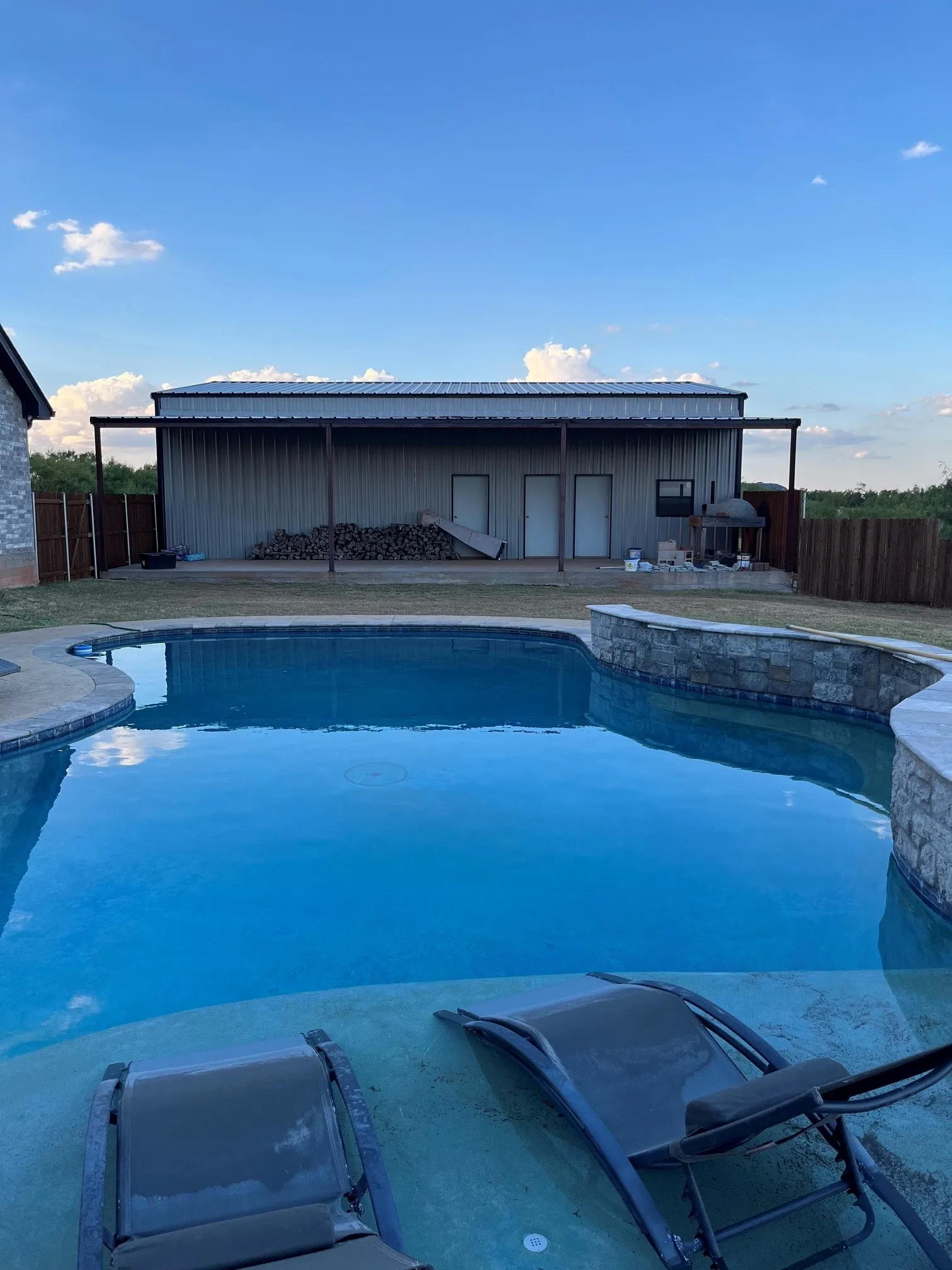 Swimming pool with curved edge, stone-clad retaining wall, and integrated concrete lounging area