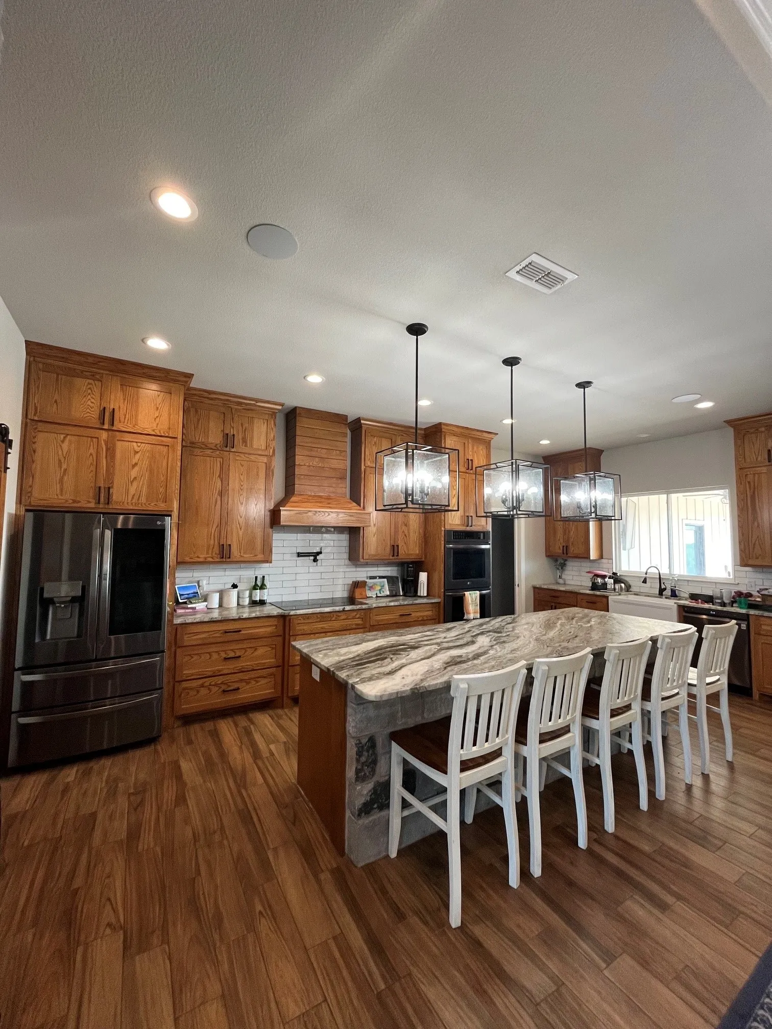 Wood-finish flooring throughout, stainless steel appliances, kitchen island with seating, pendant lighting, and recessed lighting