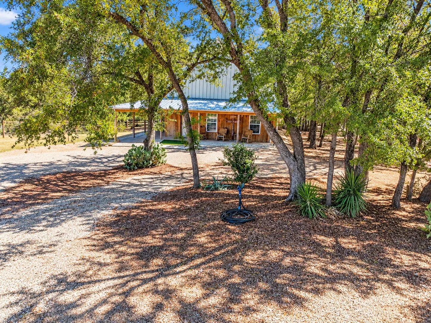Gravel driveway leading to a residence with a metal roof and full-length covered porch