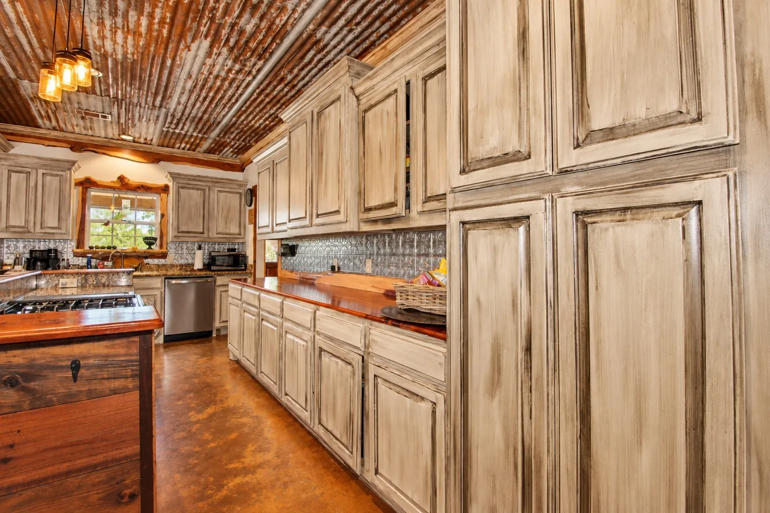 Corrugated metal ceiling, custom distressed cabinetry, rich wood countertops, stainless steel appliances, and a unique tile backsplash