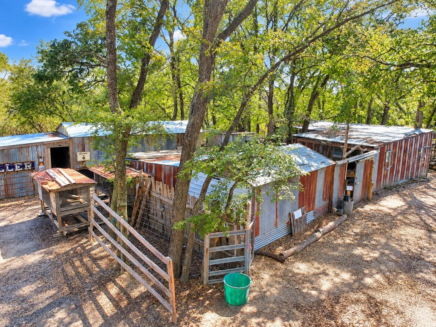 Multiple outbuildings with corrugated metal siding, wood fencing, and mature trees