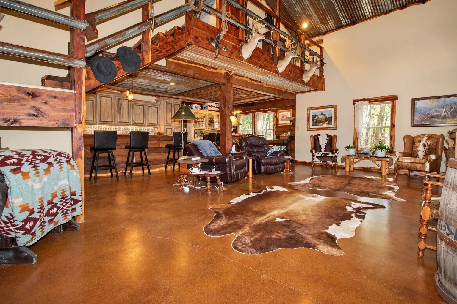 Vaulted corrugated metal ceiling, exposed wood beams, stained concrete flooring, built-in bar with cabinetry, and wood-framed windows