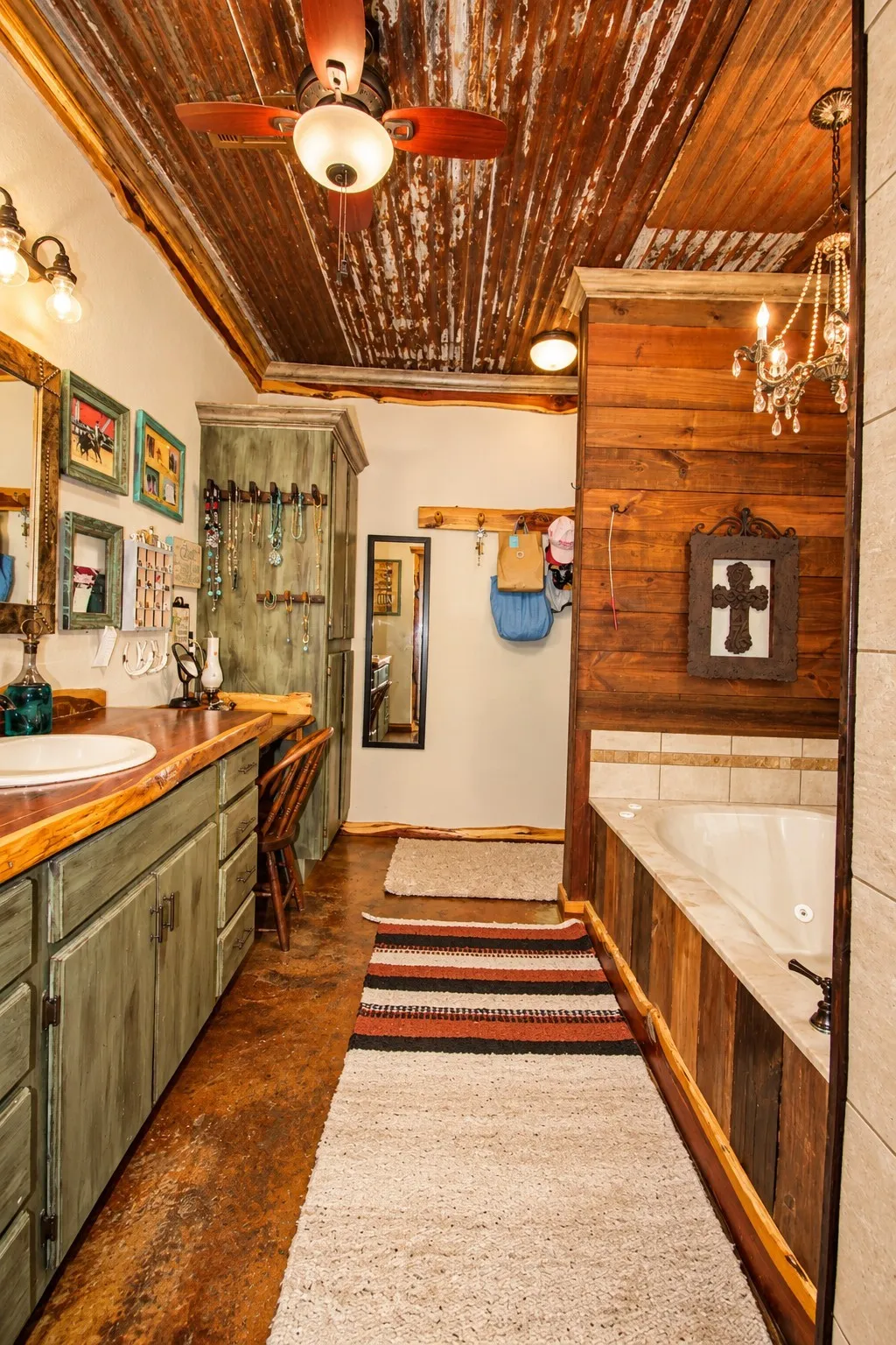 Distressed metal ceiling with a ceiling fan, dual vanity with a wood countertop, built-in soaking tub, and wood paneling