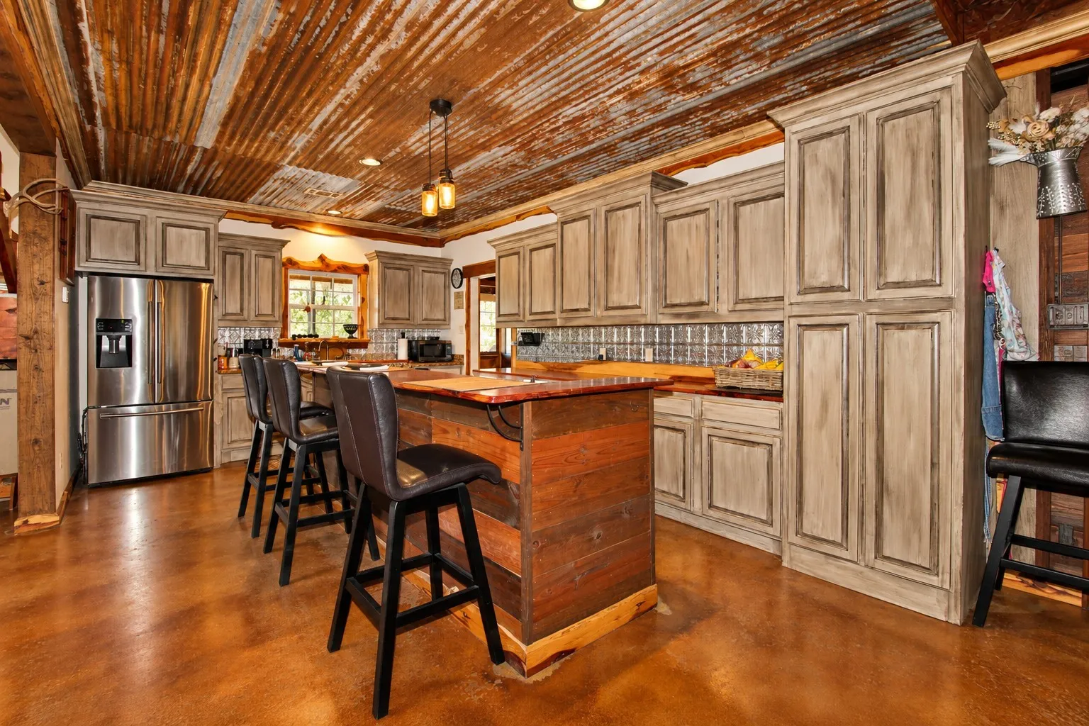 Kitchen featuring a corrugated metal ceiling, wood-finish flooring, custom cabinetry with a distressed finish, a center island with a wood base, and a tiled backsplash