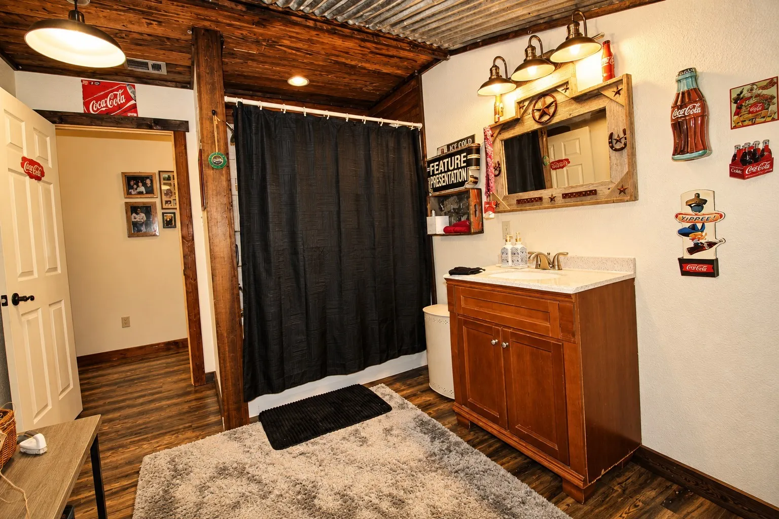 Wood-finish flooring, corrugated metal ceiling, wood plank ceiling, wood vanity with a stone-finish countertop, and a built-in vanity light fixture