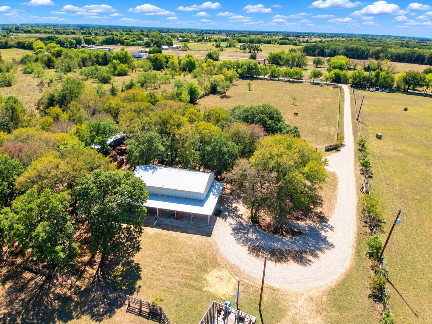 Expansive property featuring a gravel driveway, mature trees, open land, and a single-story structure with a covered porch