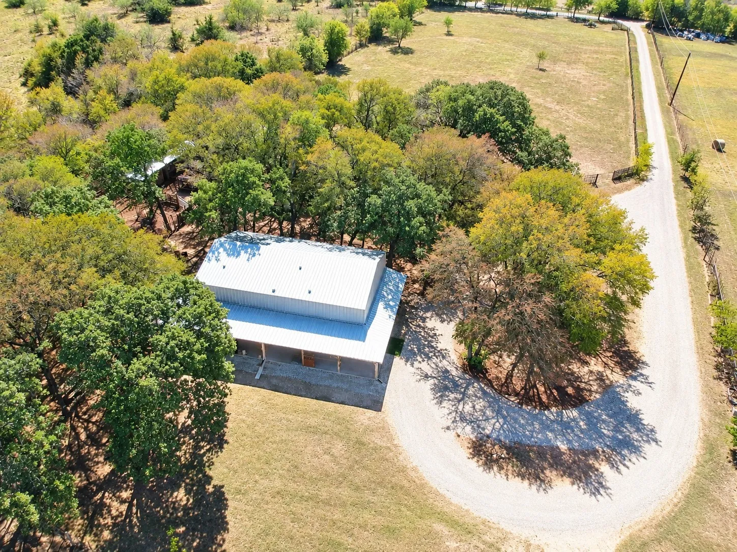 Expansive property featuring a metal roof structure, a gravel driveway, and mature trees