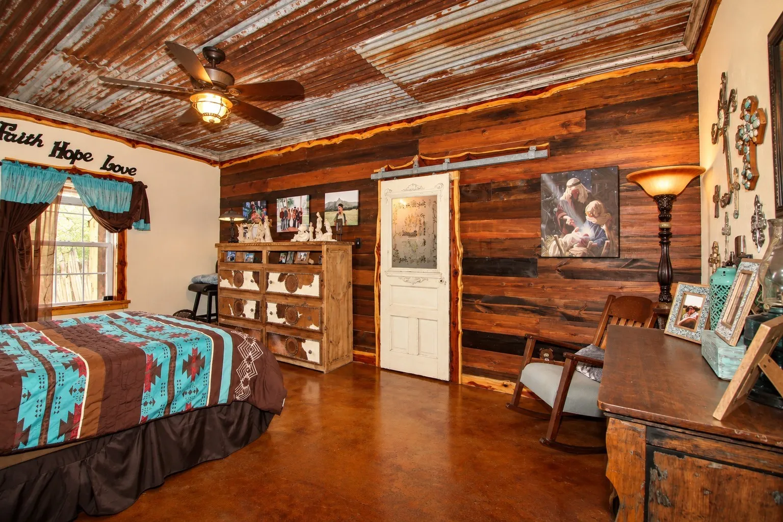 Corrugated metal ceiling with a ceiling fan, wood plank wall paneling, stained concrete flooring, and a sliding barn door