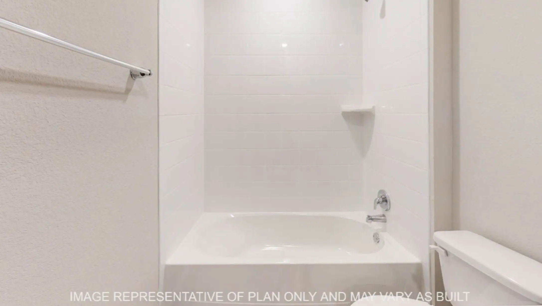 Bathtub with white tile surround and integrated shelving, chrome fixtures, and a white toilet
