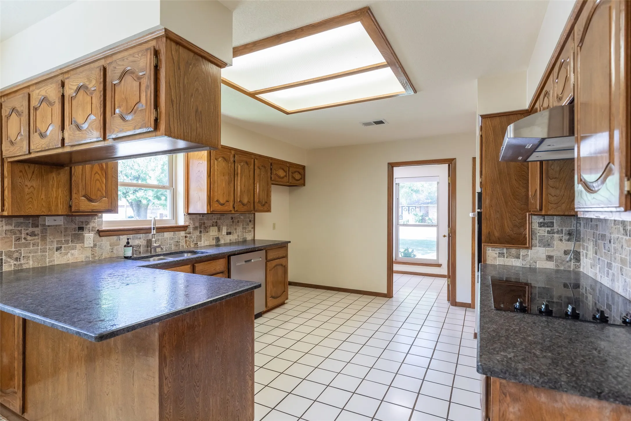 Kitchen featuring wood cabinetry, stone countertops, stainless steel appliances, tile flooring, and a recessed ceiling light fixture