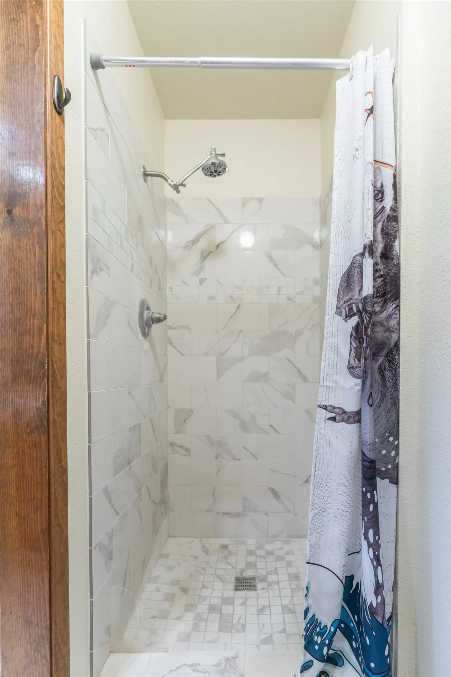 Shower with white and gray tiled walls, a mosaic tile floor, and a brushed nickel showerhead