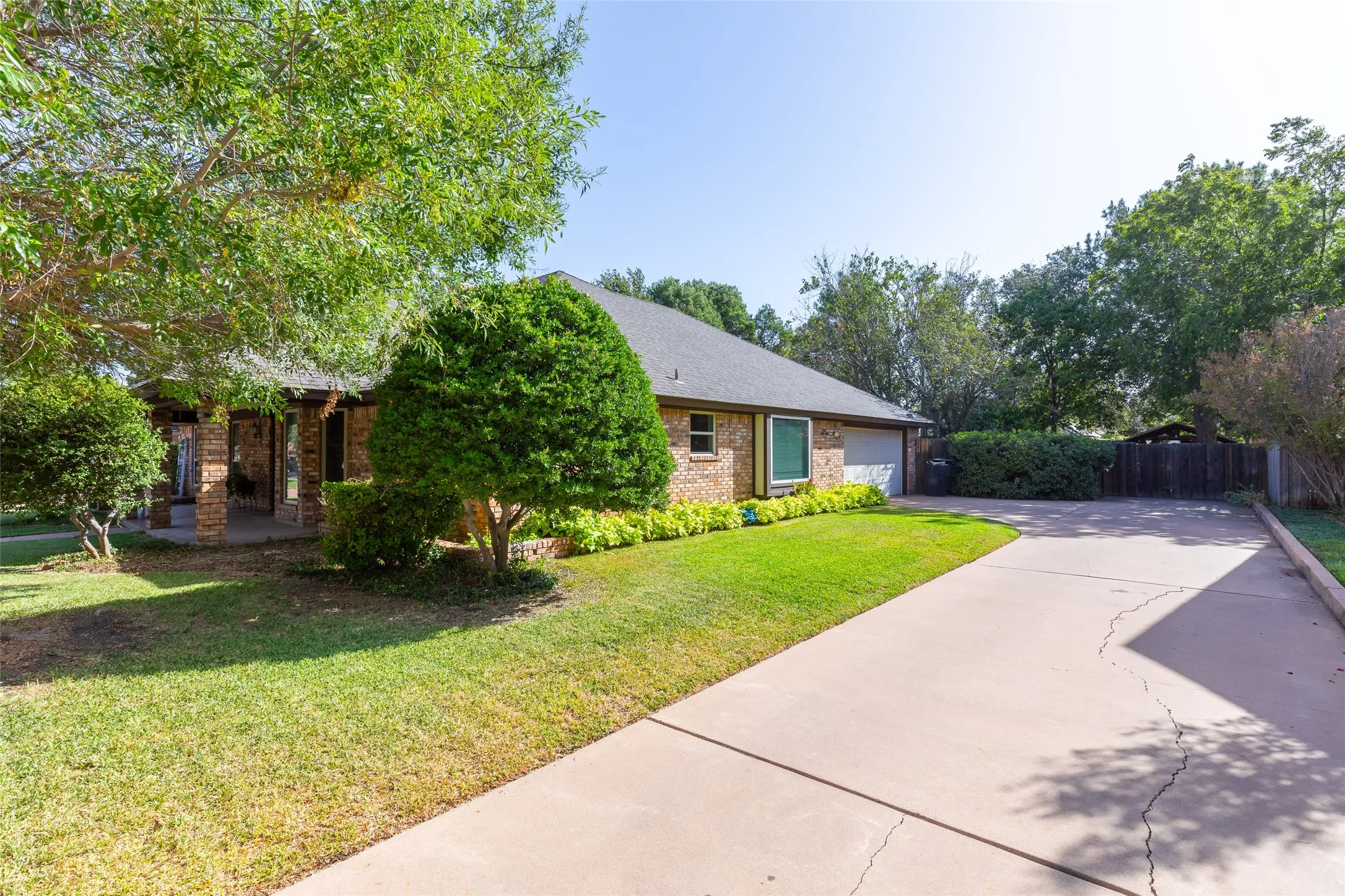 Brick exterior, covered front porch with stone columns, attached garage, concrete driveway, and established landscaping