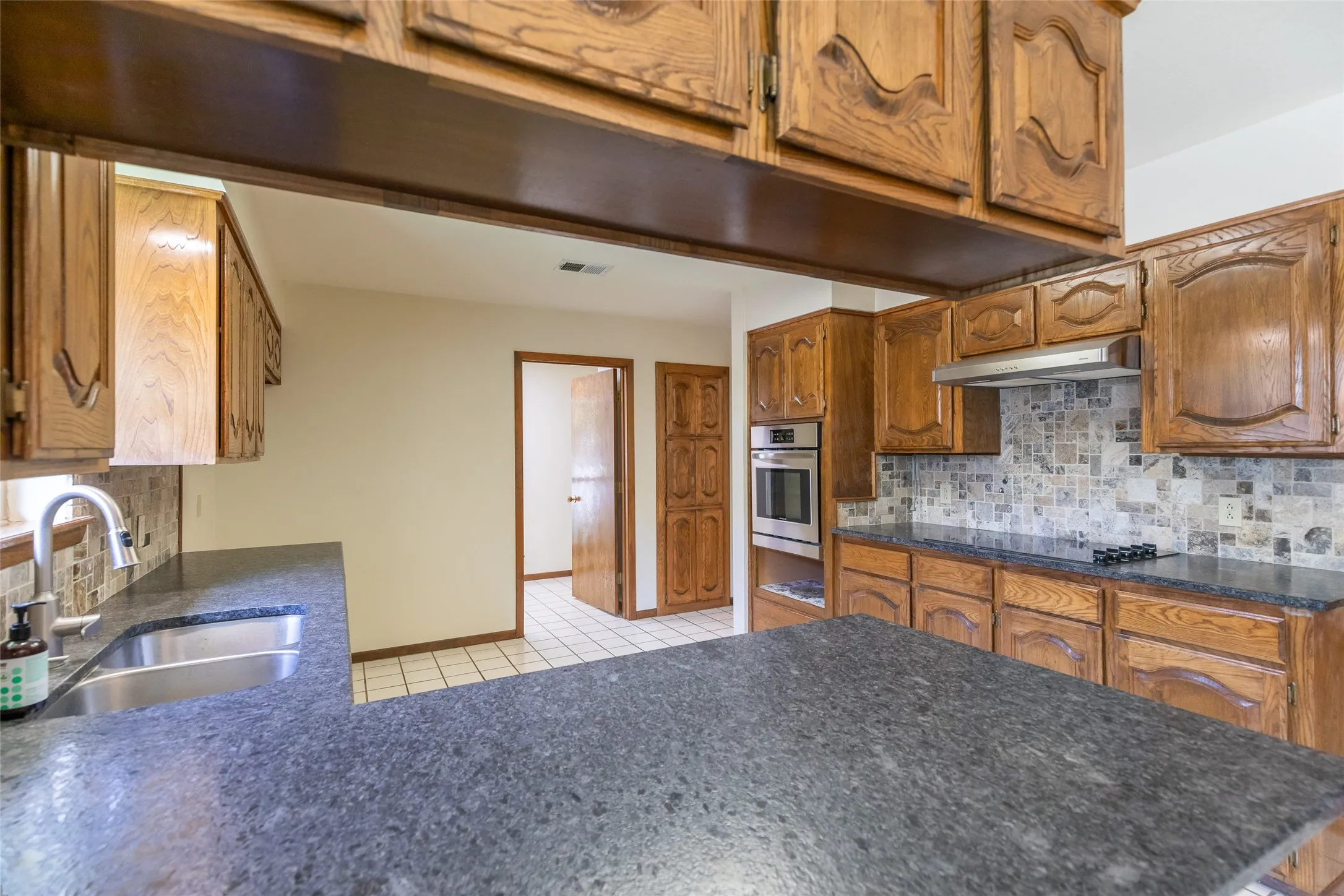 Kitchen featuring wood cabinetry, dark stone-finish countertops, and a mosaic tile backsplash