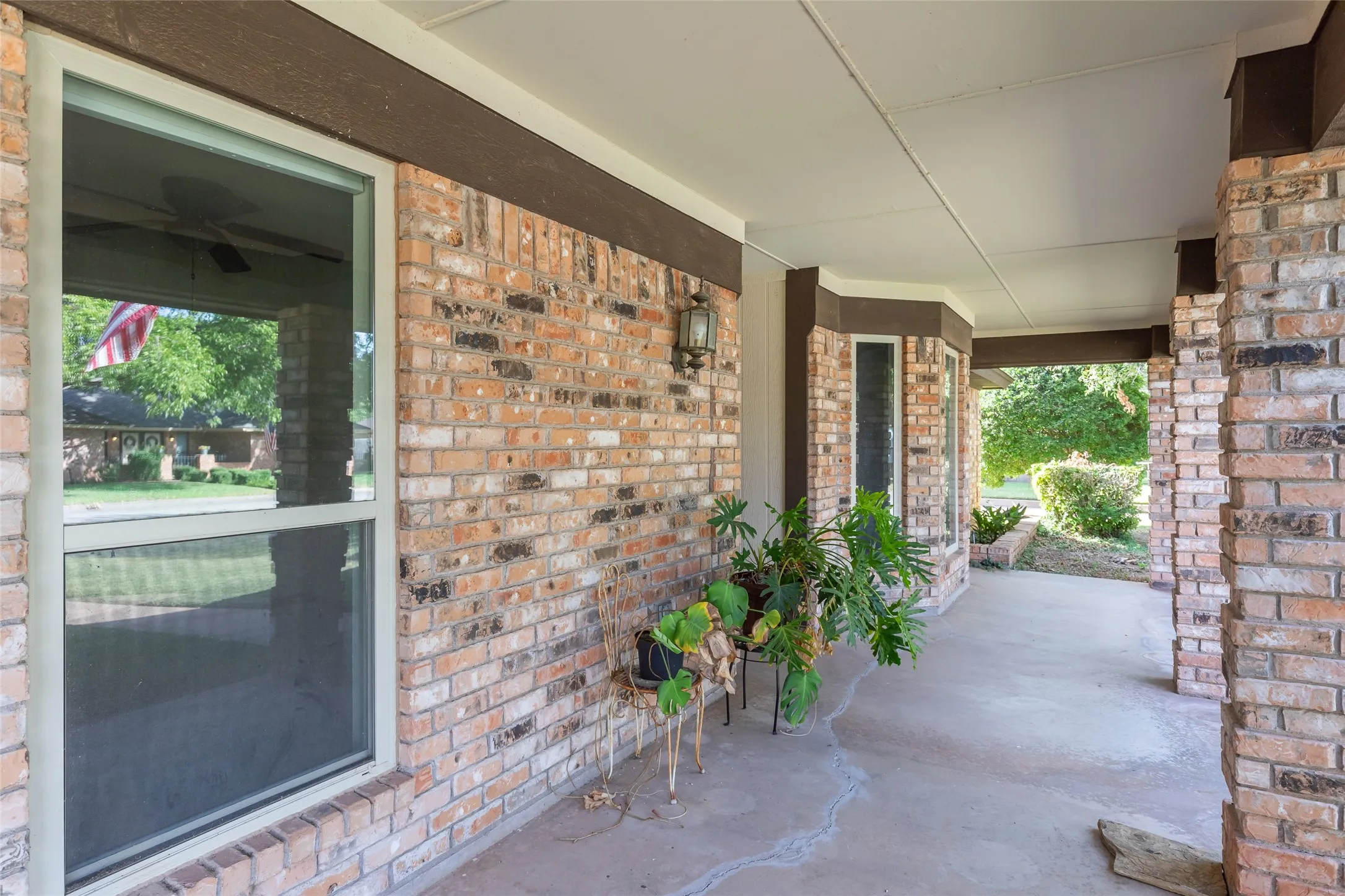 Full brick exterior with covered patio, concrete flooring, and exterior lighting fixture
