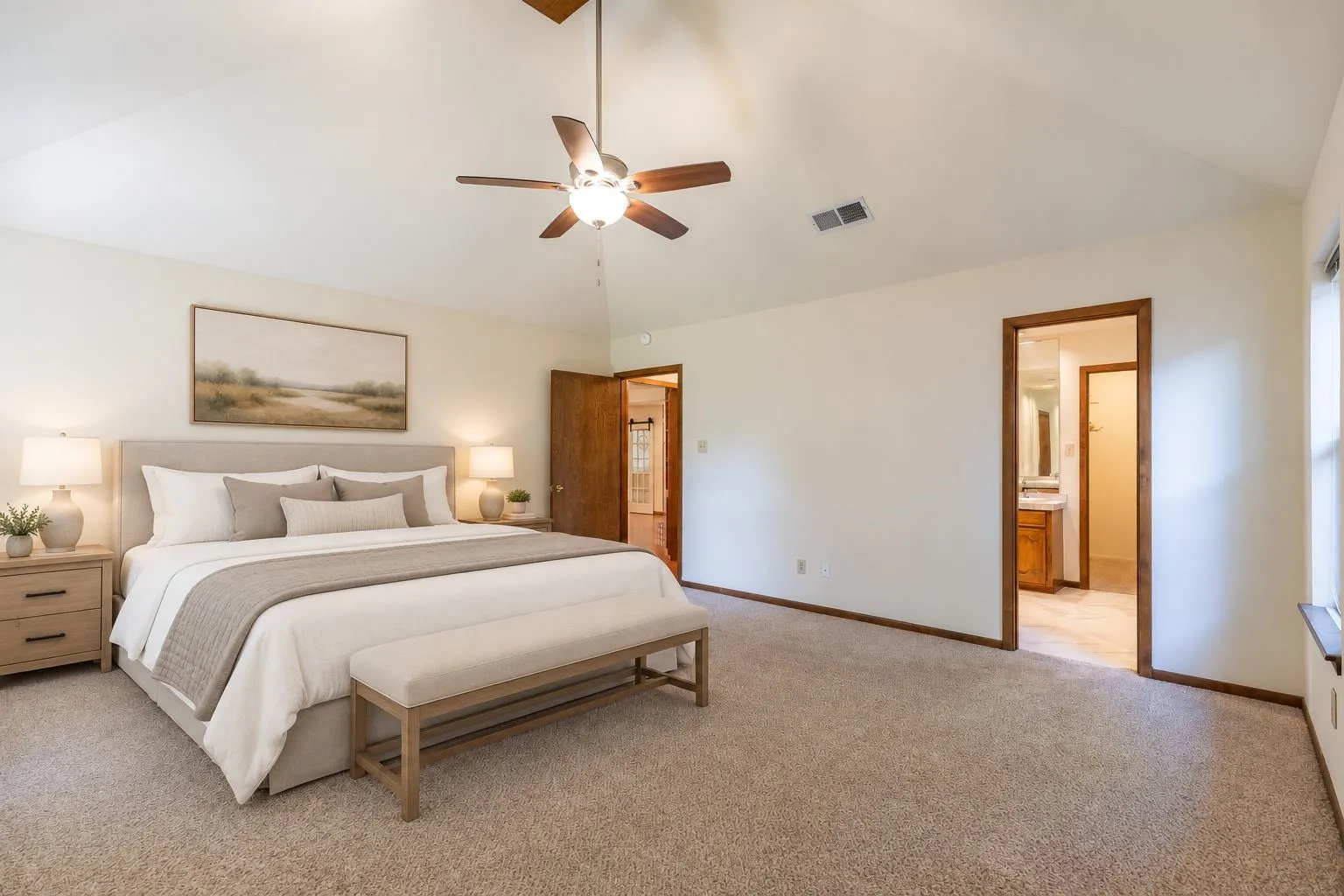 Vaulted ceiling with a ceiling fan, carpeted flooring, wood-finish trim, and direct bathroom access