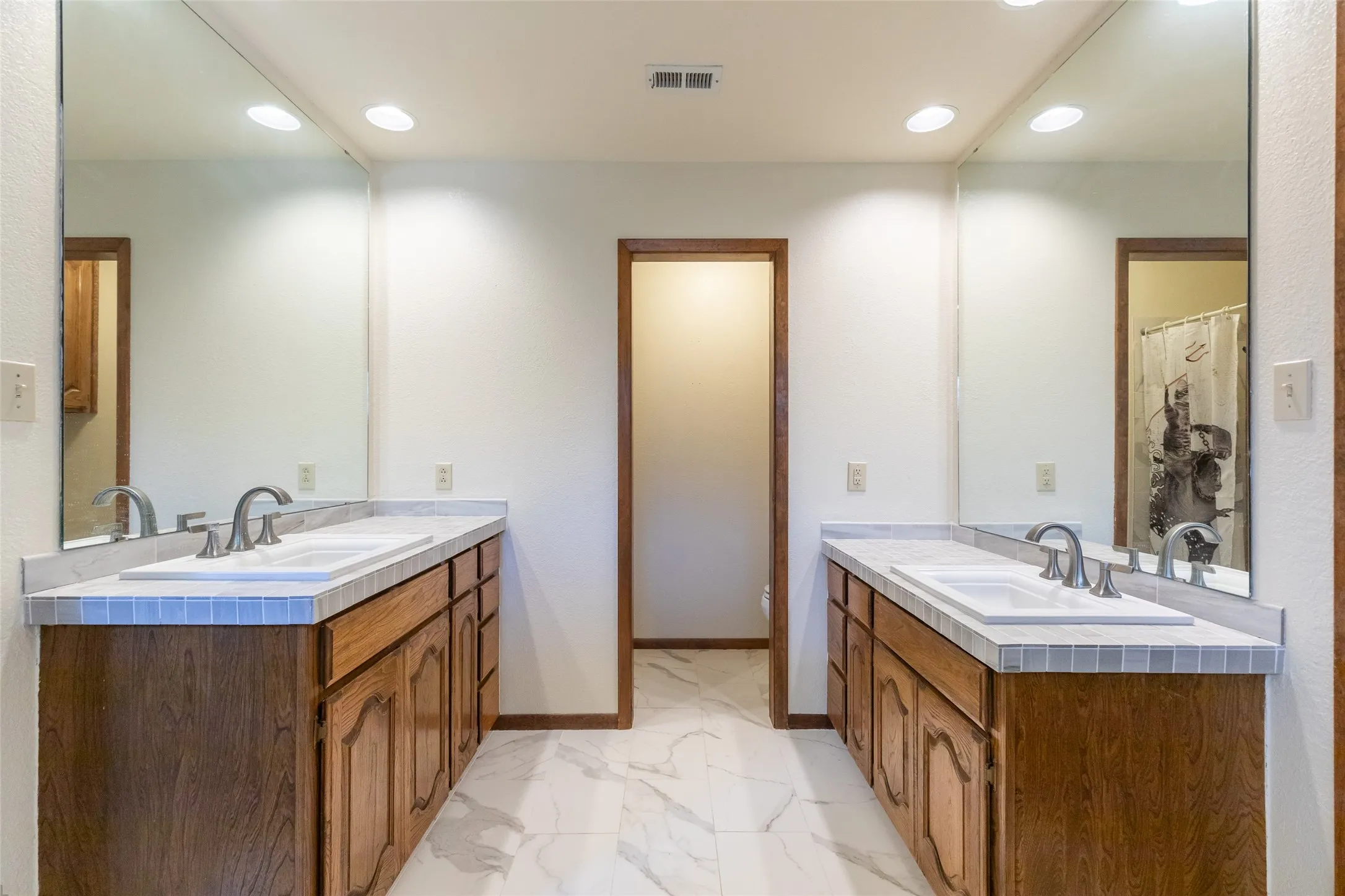 Dual vanities with wood cabinetry, integrated sinks, chrome fixtures, and tiled countertops